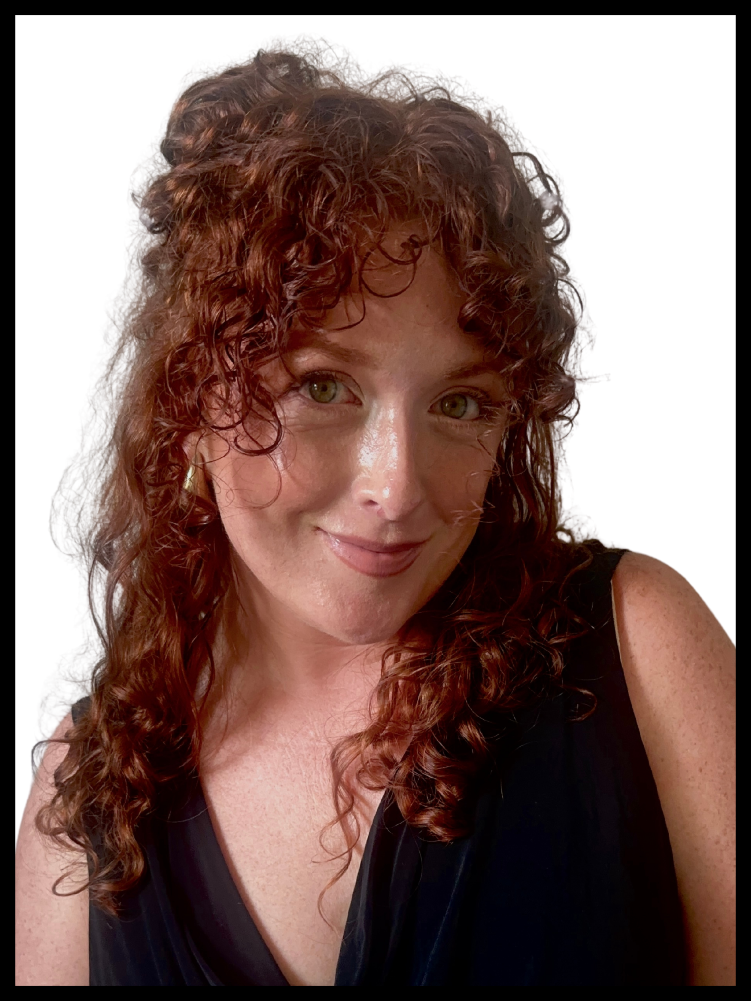 A woman with long, curly red hair and green eyes is smiling gently at the camera. She is wearing a black sleeveless top, and the background is plain white.