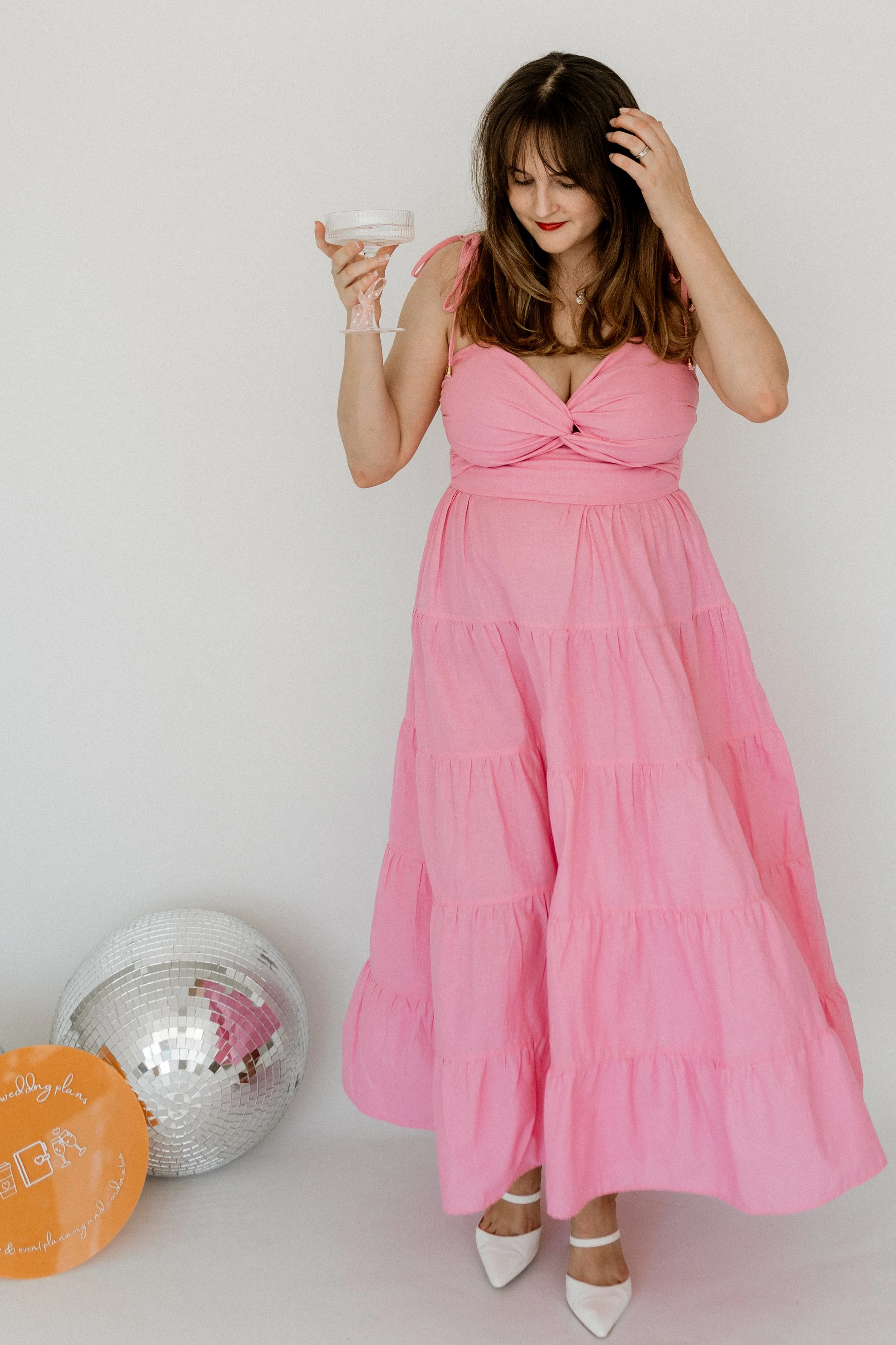 Woman in a pink dress holding a glass with balloons nearby.