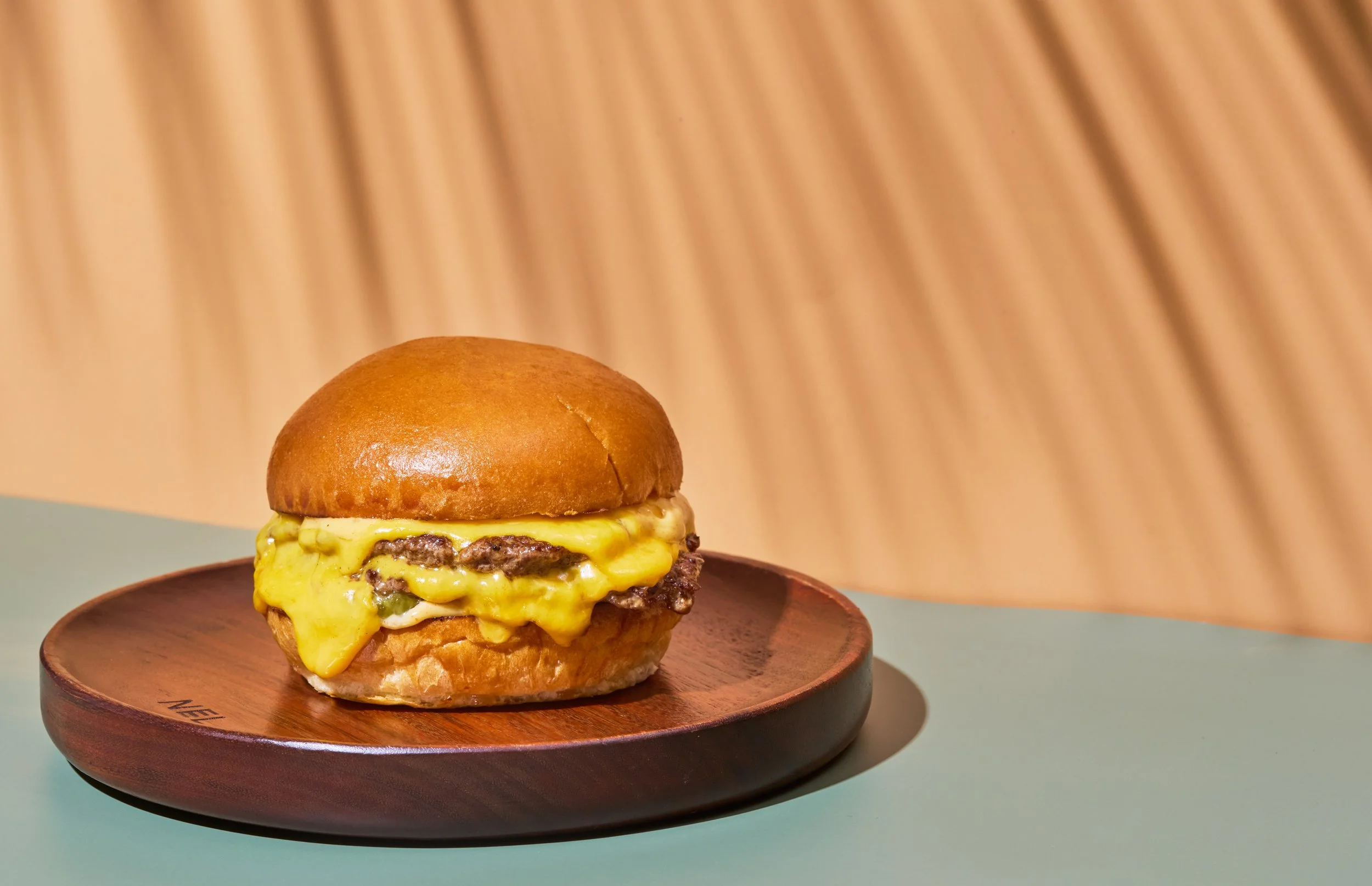 Close-up of a cheeseburger with melted cheese, lettuce, and beef patty on a wooden plate, with a wooden textured background.