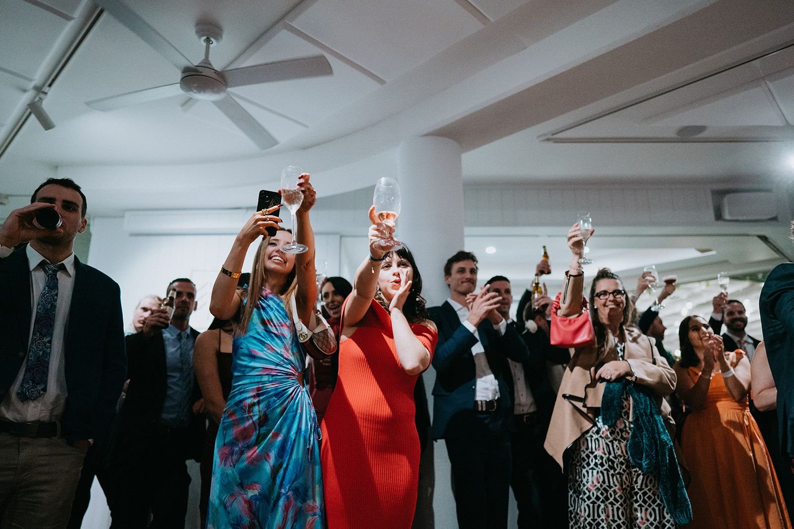 Group of people celebrating with drinks, some raising glasses in a toast, at an indoor event.