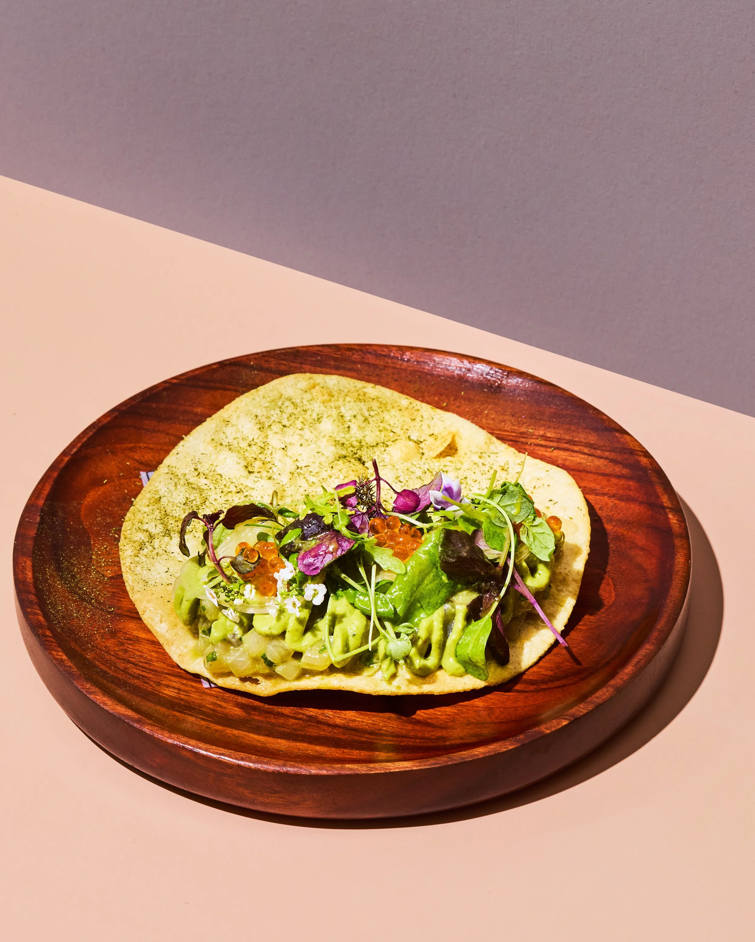 A pizza topped with various fresh greens and garnishes on a wooden plate.