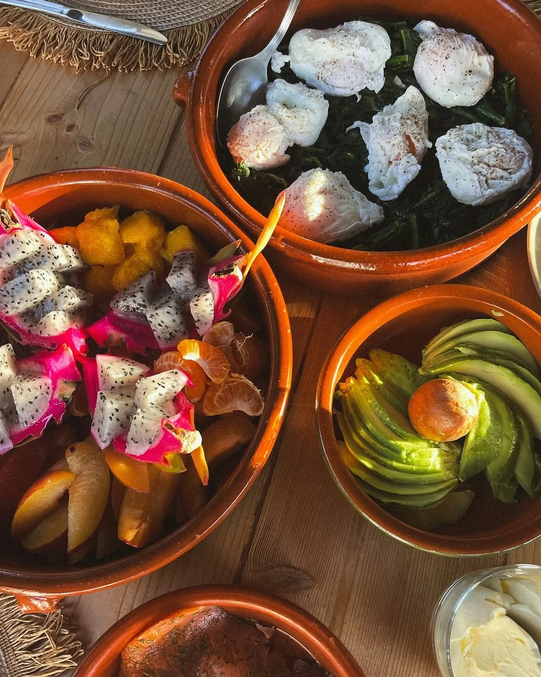 Three bowls of food with poached eggs, dragon fruit, avocado, and other fresh ingredients on a wooden table.