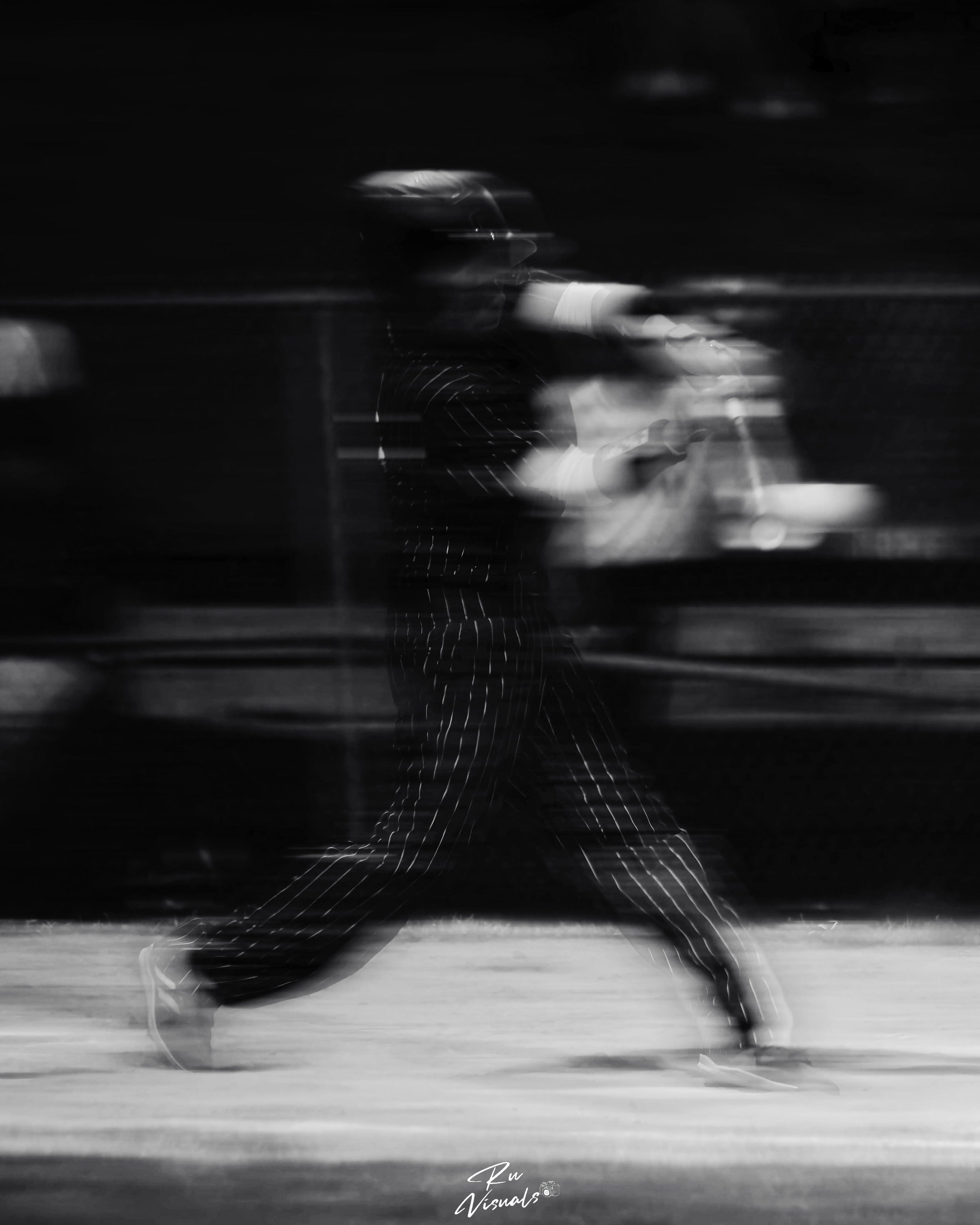 Black and white photo of a person running on an outdoor track or pavement, wearing sunglasses and a striped shirt, with motion blur.