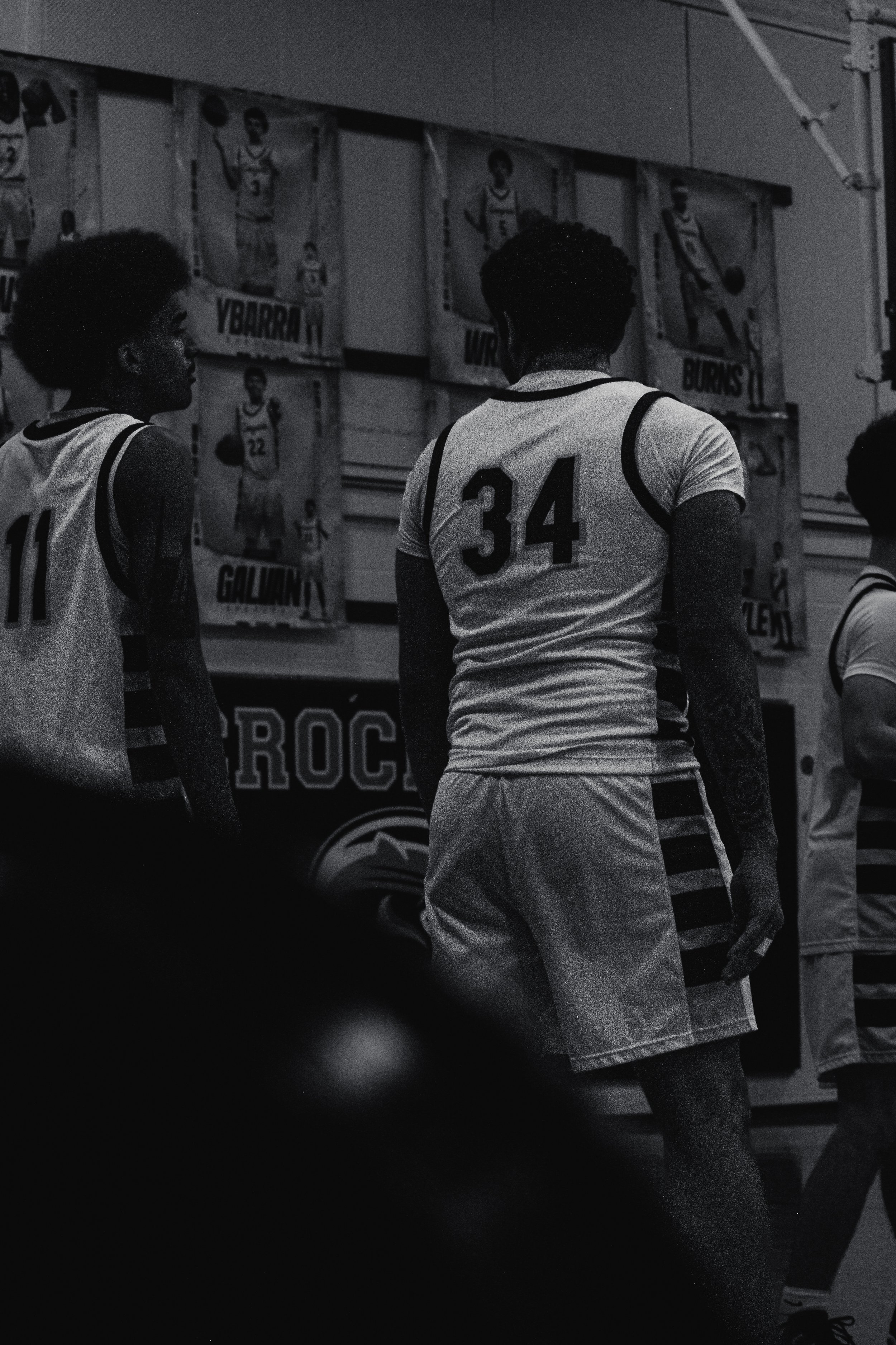 A group of basketball players standing inside a gymnasium, facing posters of basketball players on the wall.