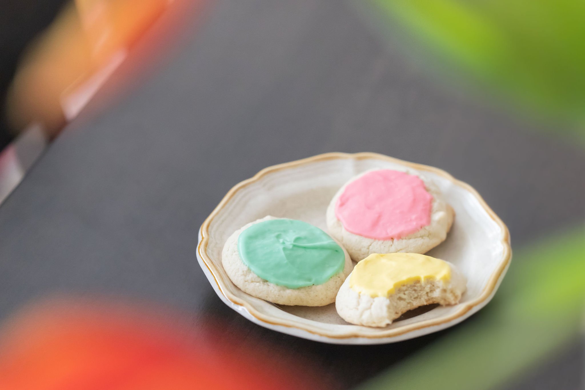 Product photography of a plate with three cookies decorated with pink, green, and yellow icing.