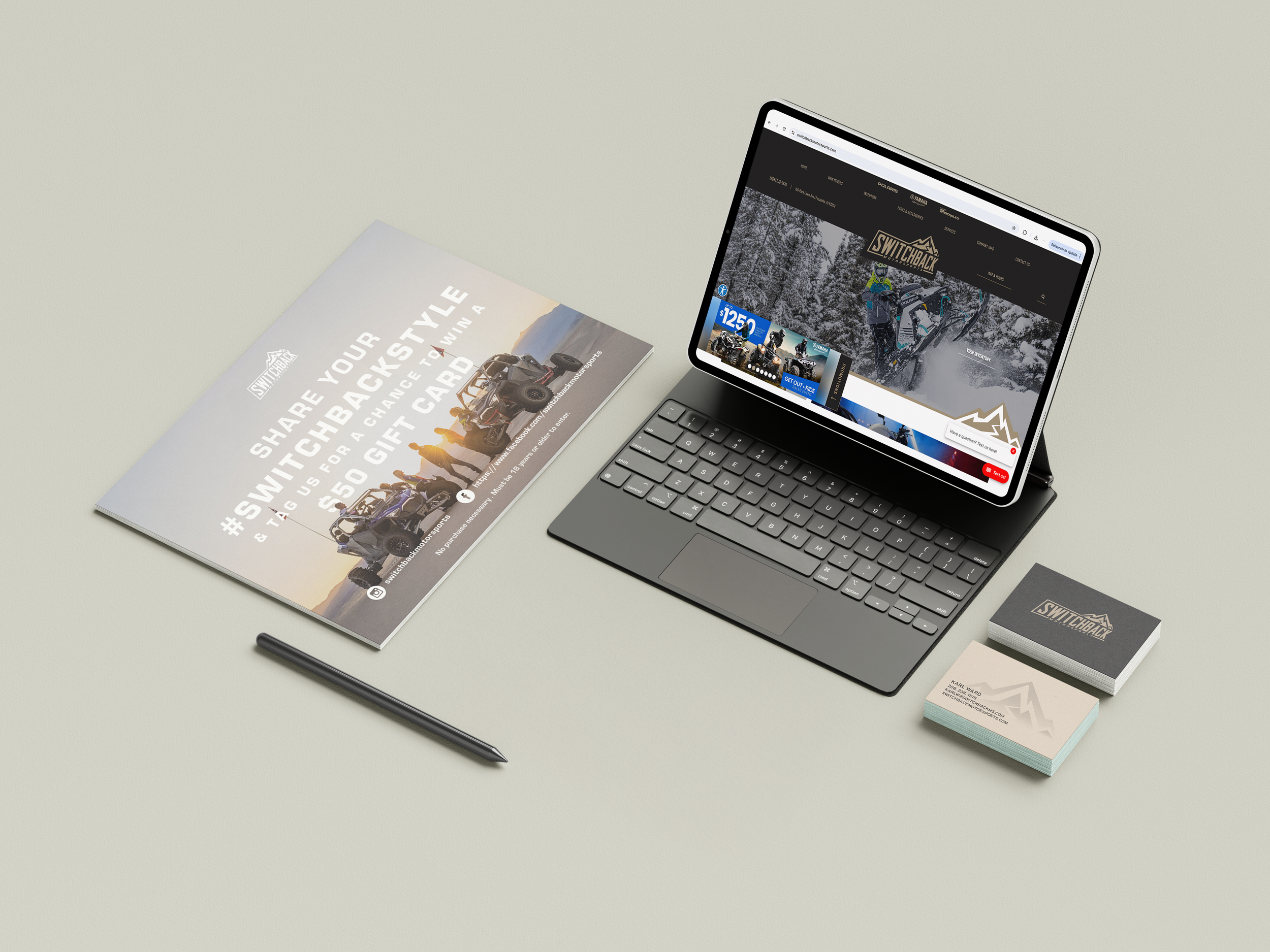 A digital tablet with a keyboard displaying the Switchback Outdoors website, a business card and a stack of cards with the Switchback logo, a brochure encouraging sharing a Backstyle hashtag for a chance to win a gift card, and a stylus pen on a light gray surface.