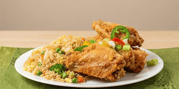 Plate of fried chicken with a side of fried rice and mixed vegetables, garnished with sliced green chili