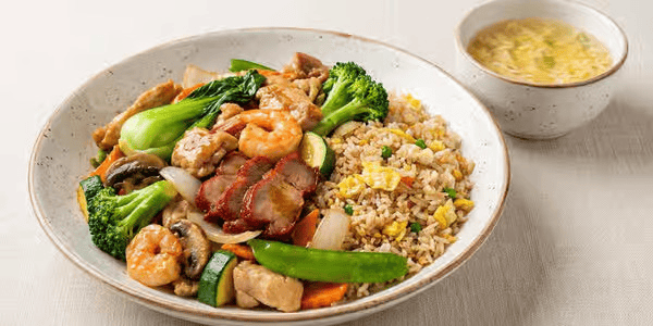 Stir-fried vegetables with shrimp and chicken served with fried rice and a bowl of egg drop soup.