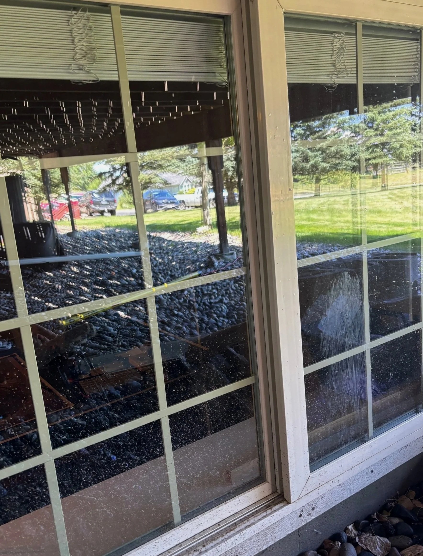 View through a glass window showing reflections of trees and parked cars outside.