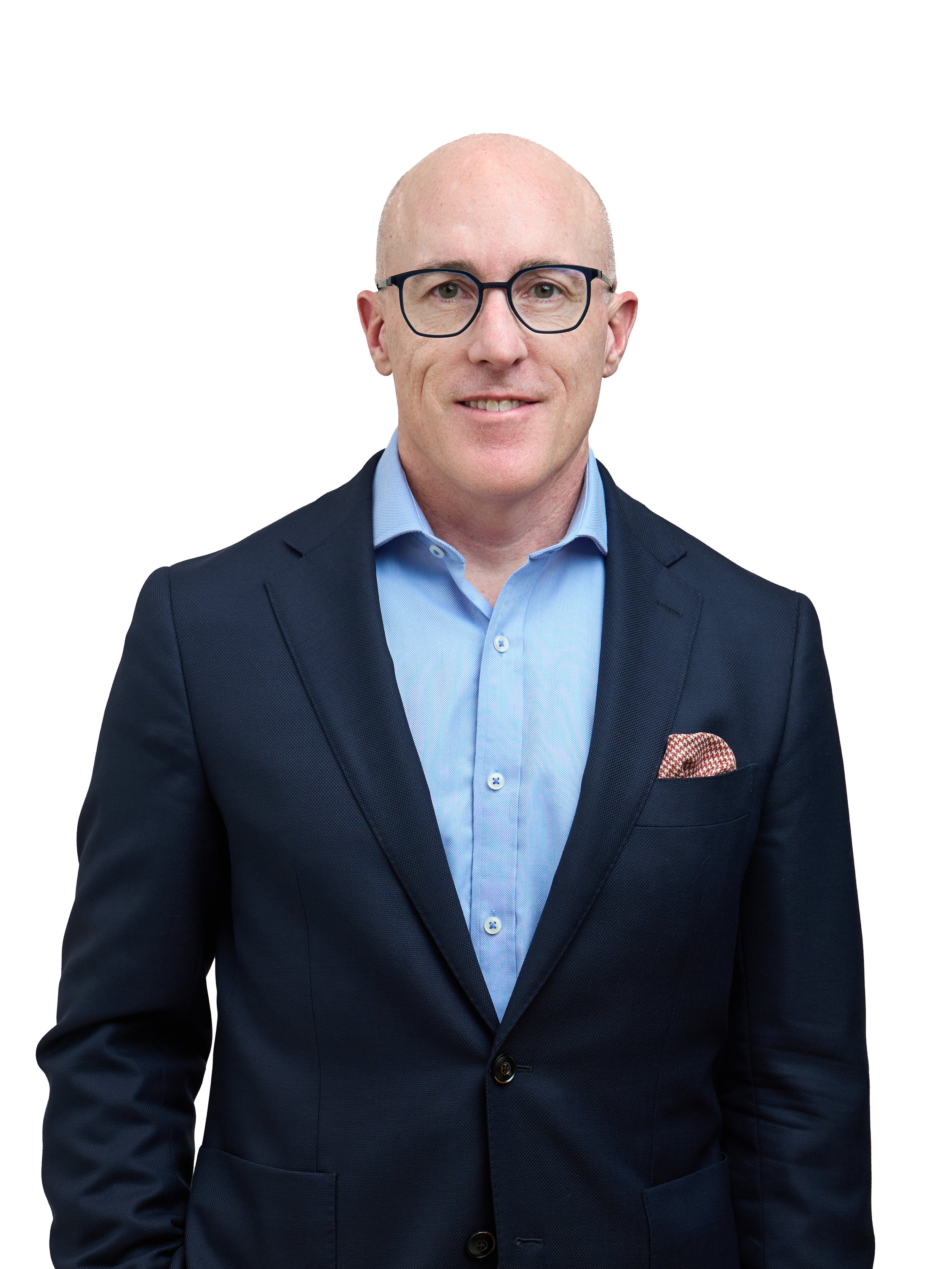 A bald man wearing glasses, a light blue shirt, a dark blue blazer, and a patterned pocket square, smiling against a plain white background.
