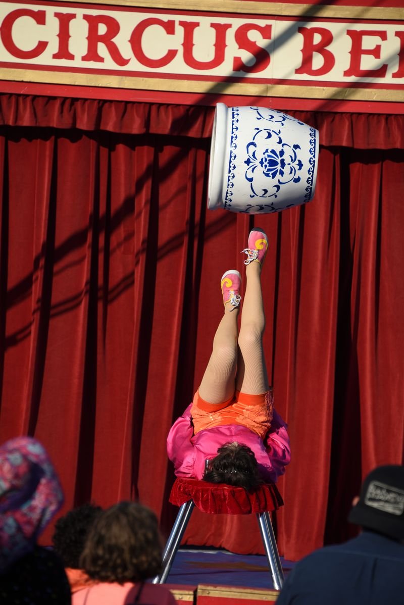 A performer foot juggling at Circus Bella balancing a large decorated jar on her feet during a circus show.
