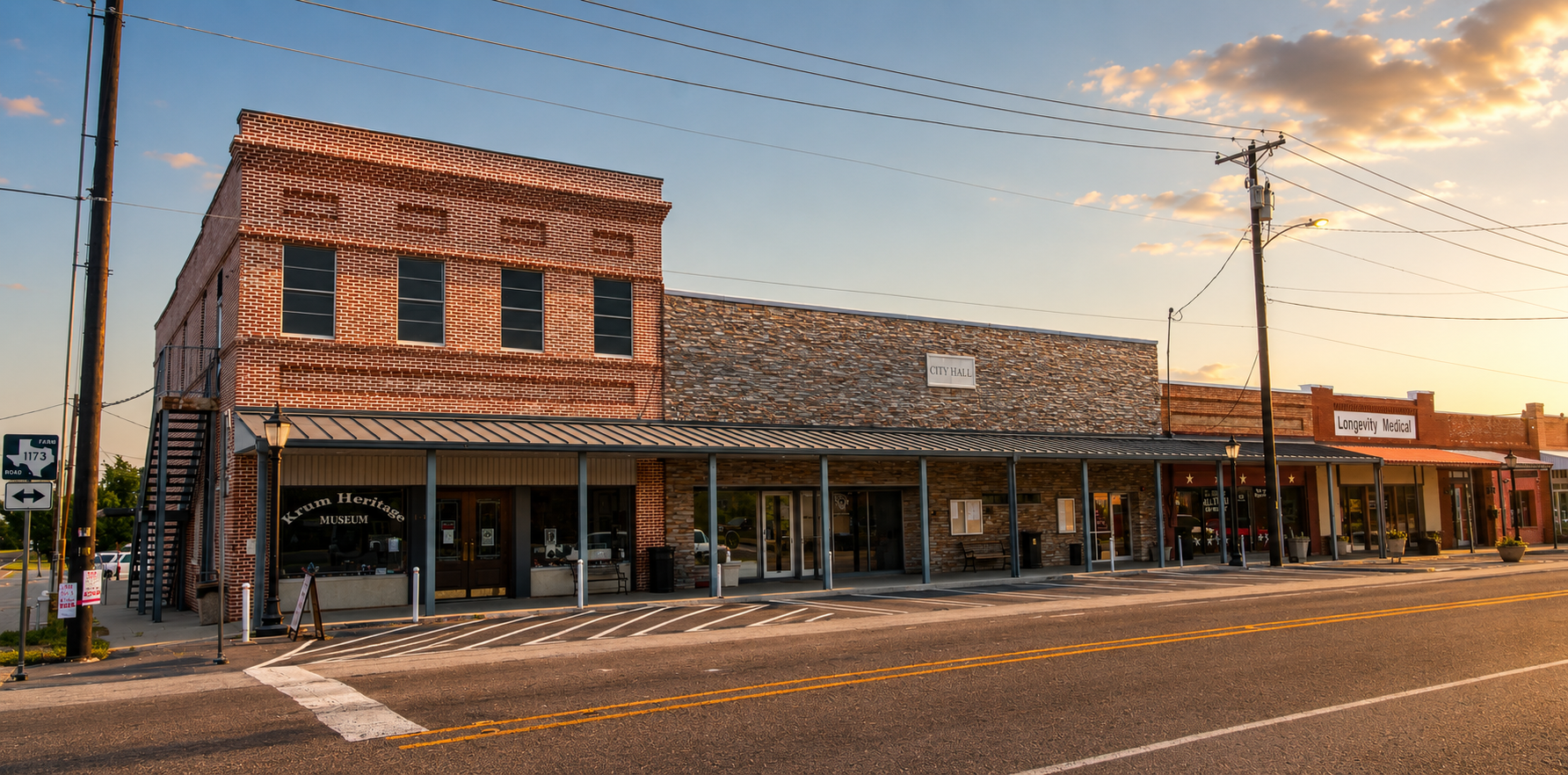 Street view of a small town with brick buildings, including a museum and medical office, during sunset. There are power lines and street lamps visible.