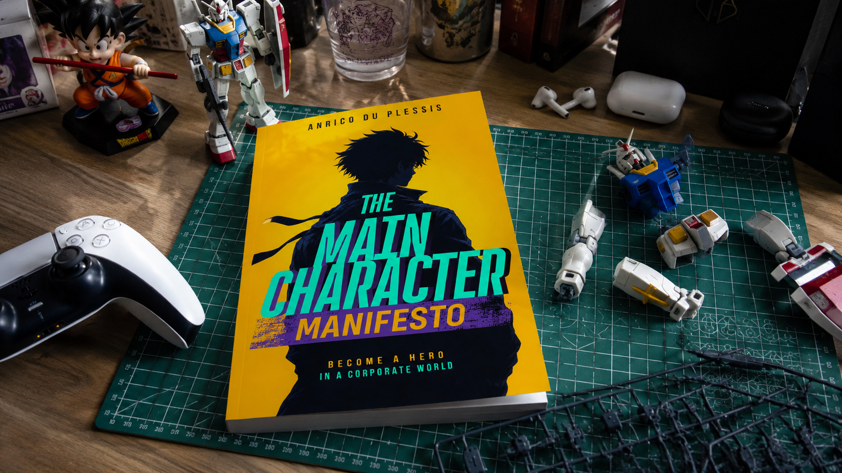 A work desk with a green cutting mat, a yellow book titled 'The Main Character Manifesto' by Anrico du Plessis, Keynote speaker, author, podcast host and CEO of Multi-Media