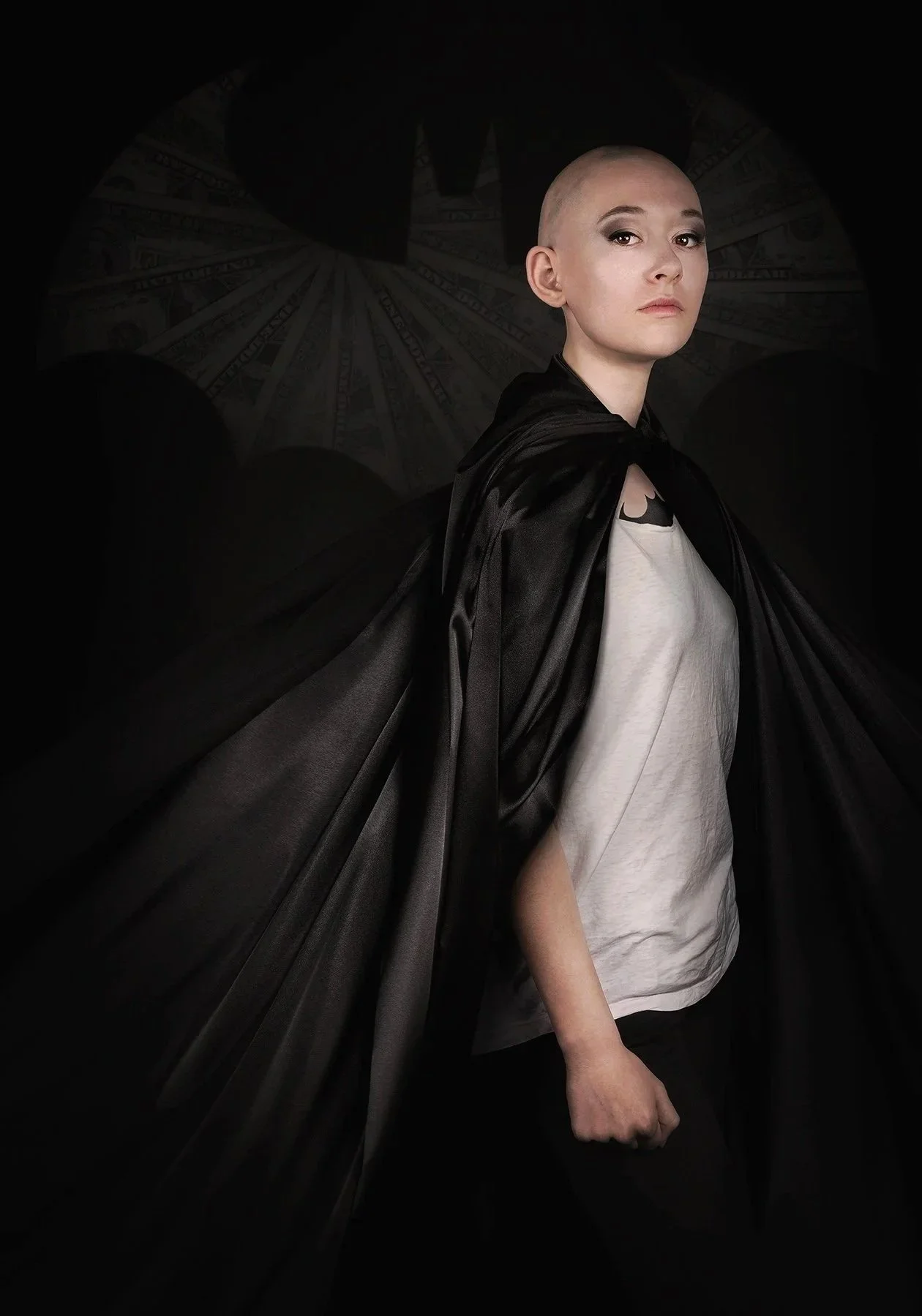 Une femme avec une tête rasée portait une cape noire, une chemise blanche et ne porte pas de maquillage, avec un fond sombre et une image de dollar en arrière-plan.