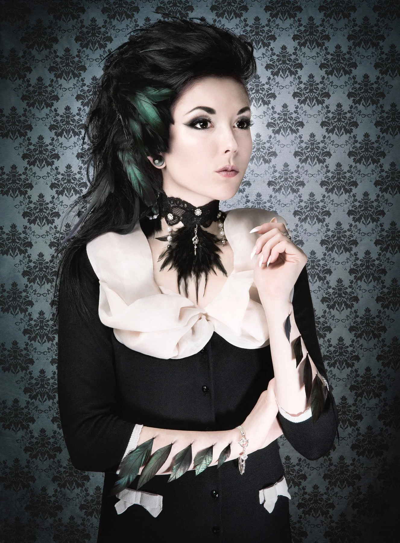 Une femme avec un cheveu violet et une robe noire, portant un collier en plumes noires et perles, se tenant devant un fond décoratif en damier.