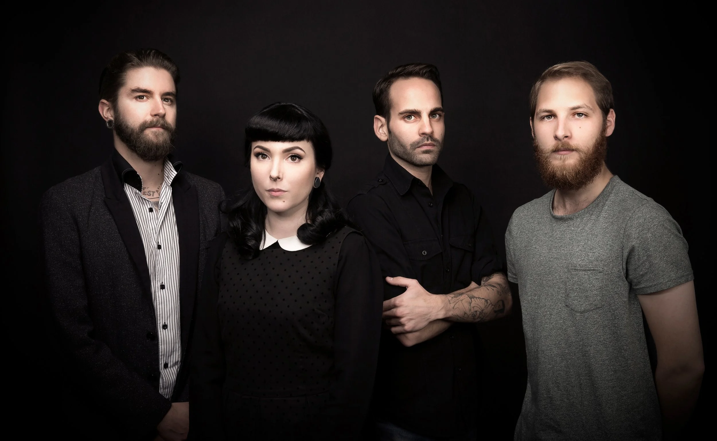 Groupe de quatre personnes posant devant un fond noir, cinq hommes et une femme avec un style alternatif, coiffures et vêtements modernes, expression sérieuse ou neutre.