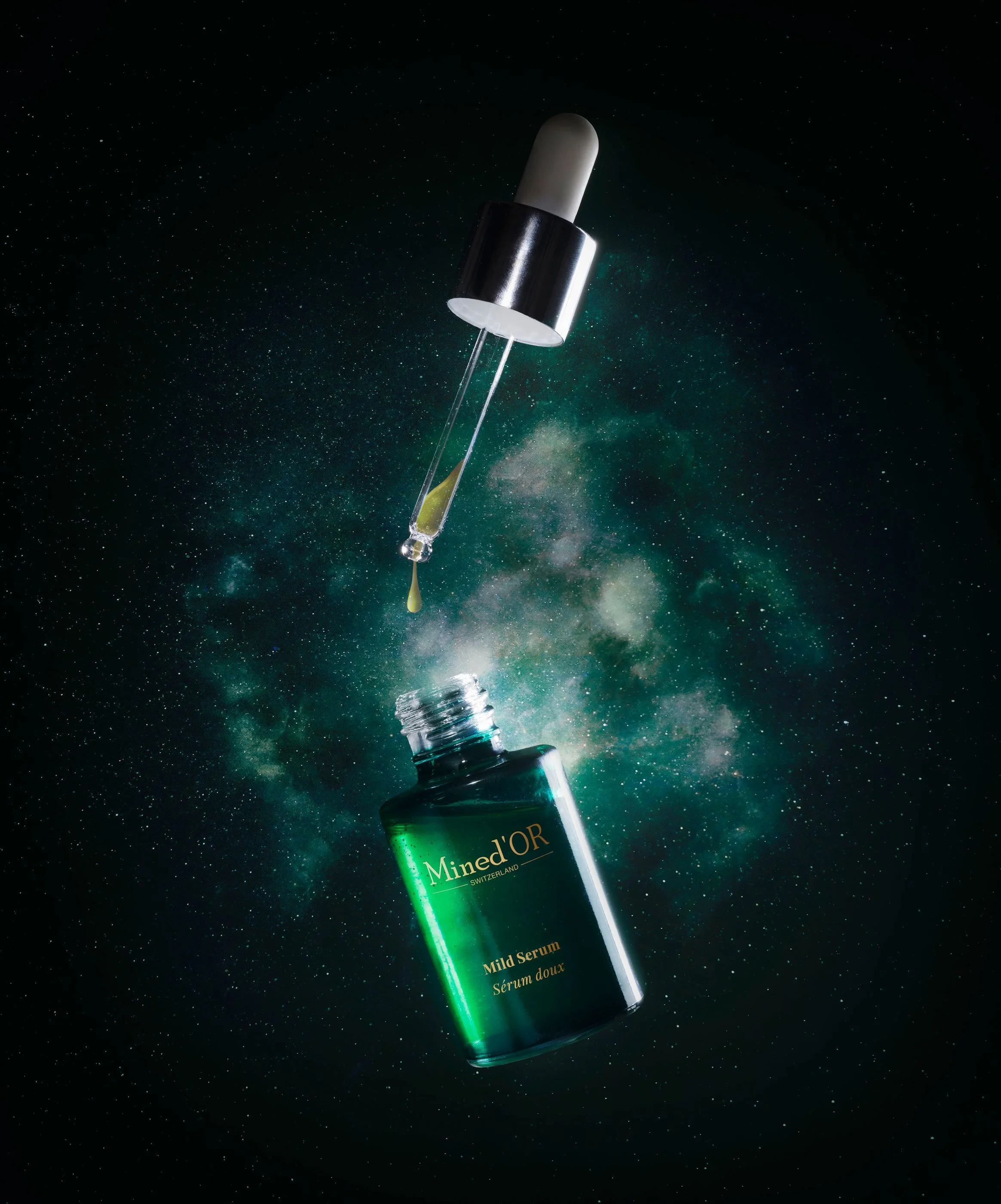 Une fiole de sérum doux Minhéd'OR en suspension dans l'espace contre un fond de galaxie et d'étoiles, avec la pipette en train de déposer quelques gouttes de sérum.