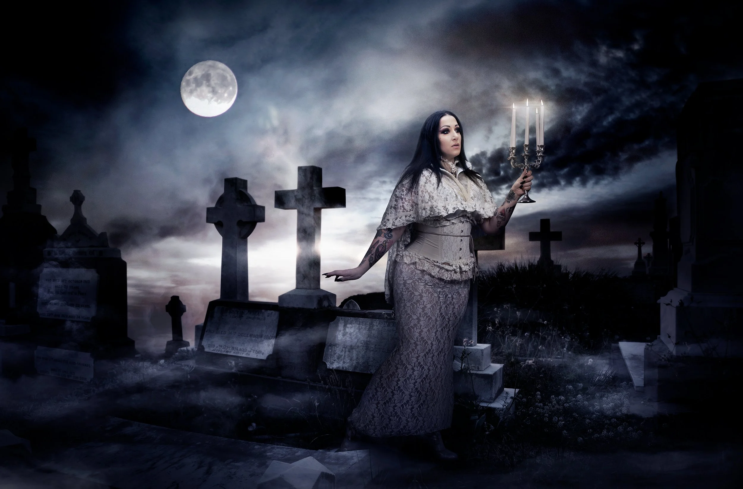Une femme en robe longue avec des tatouages, tenant un chandelier à trois branches, se tient dans un cimetière sous un ciel nocturne avec une pleine lune et des nuages sombres.