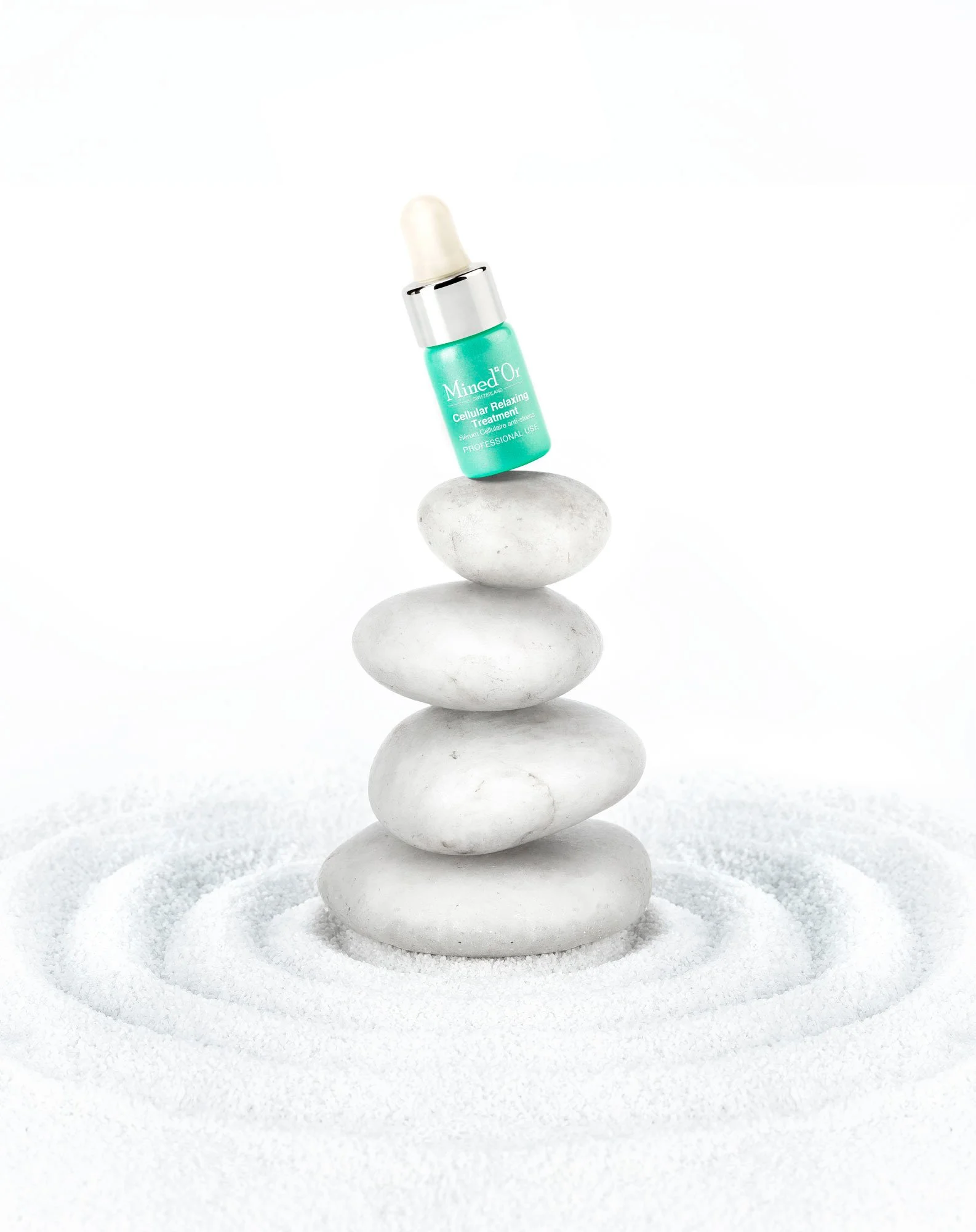Un flacon de sérum pour la relaxation cellulaire posé sur une roche, en équilibre sur d'autres roches plates, dans un décor épuré blanc.