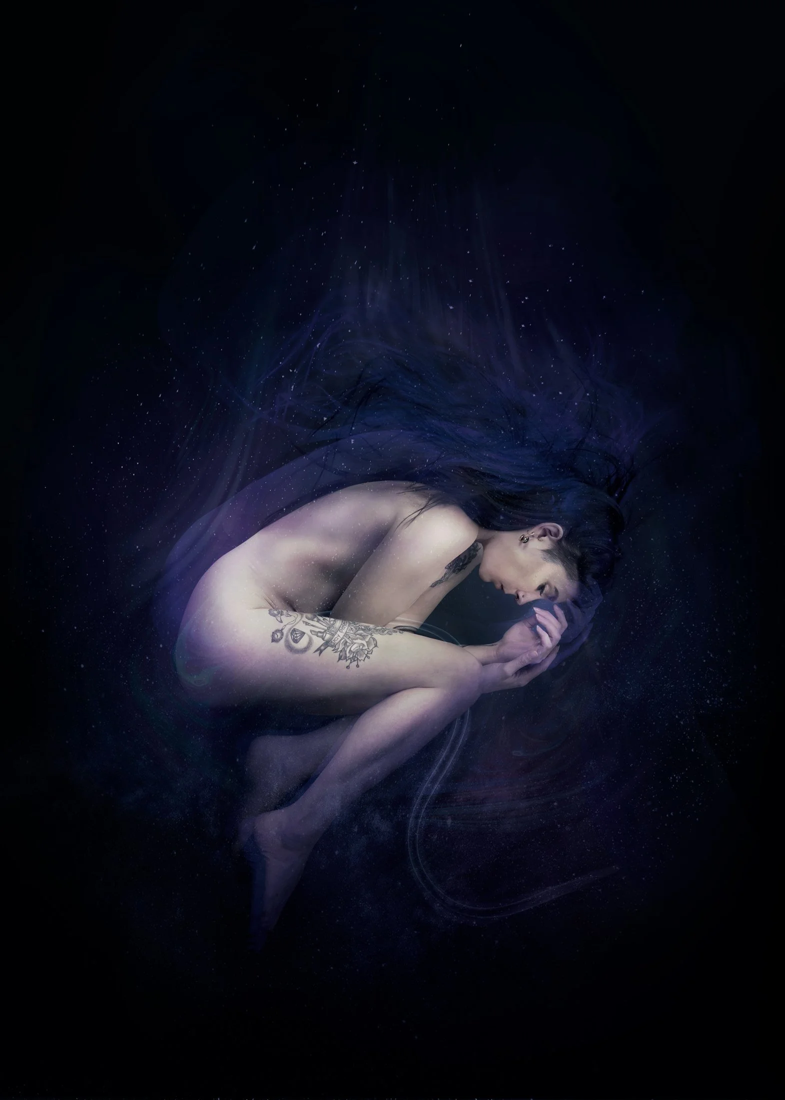 Une jeune femme nue, pliée en position de fetal, flottant dans l'espace avec un fond noir rempli de petites étoiles. Elle a des tatouages sur le bras et des piercings à l'oreille.