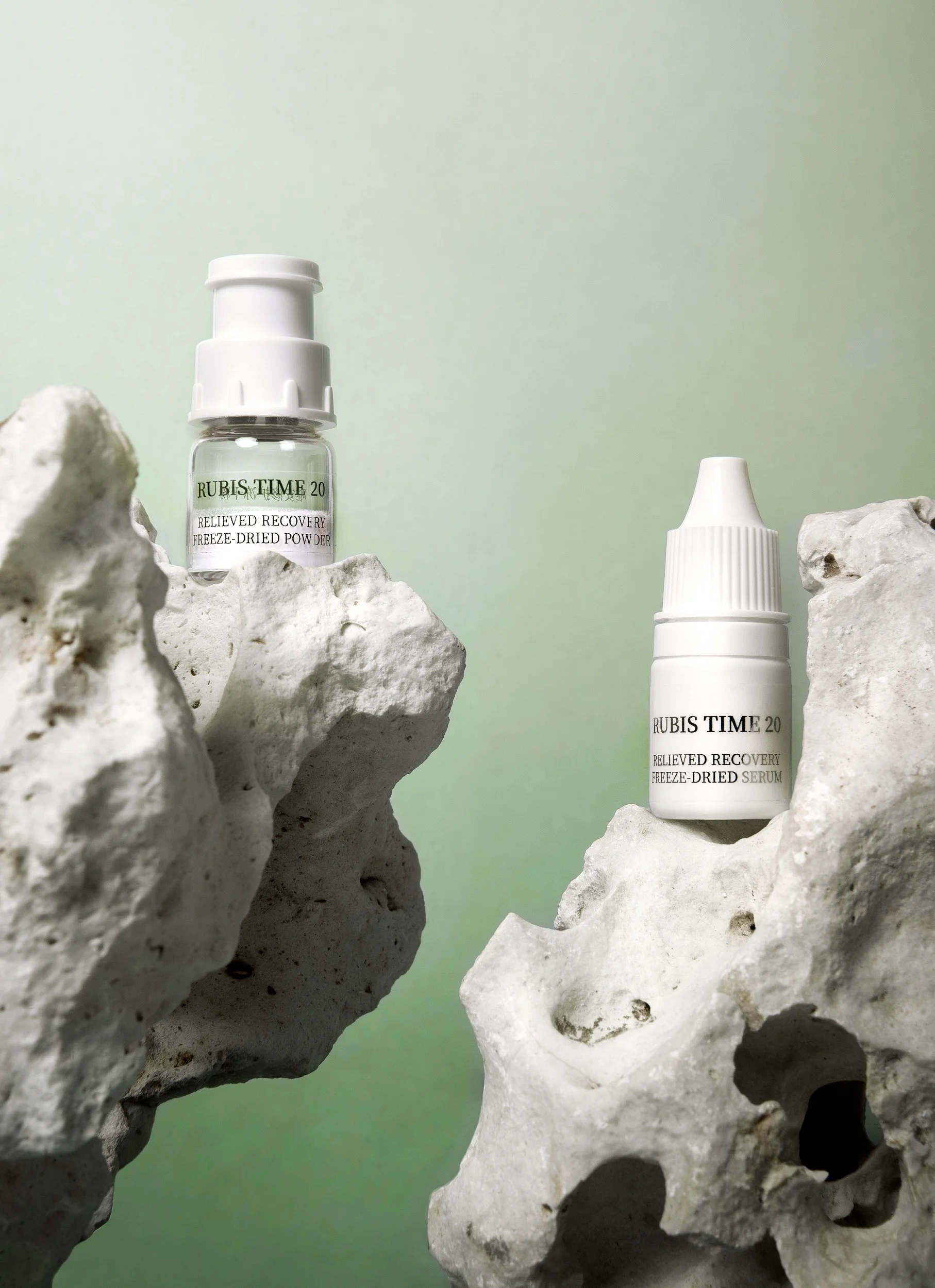 Deux flacons de produits cosmétiques blancs posés sur des roches blanches avec un fond vert pâle.