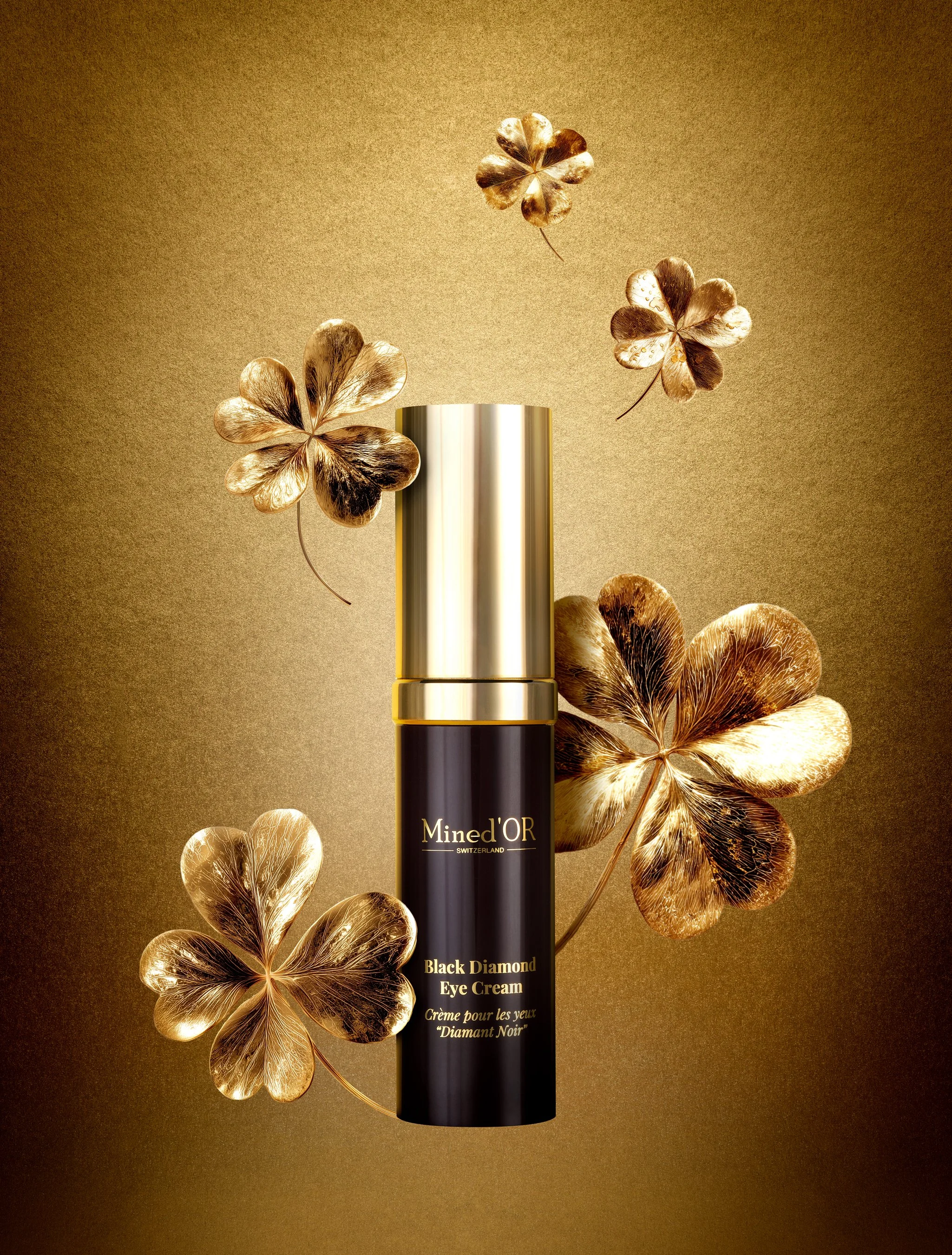 Un flacon de crème pour les yeux noir diamant de la marque Mined'OR Switzerland, entouré de feuilles dorées en forme de trèfle
