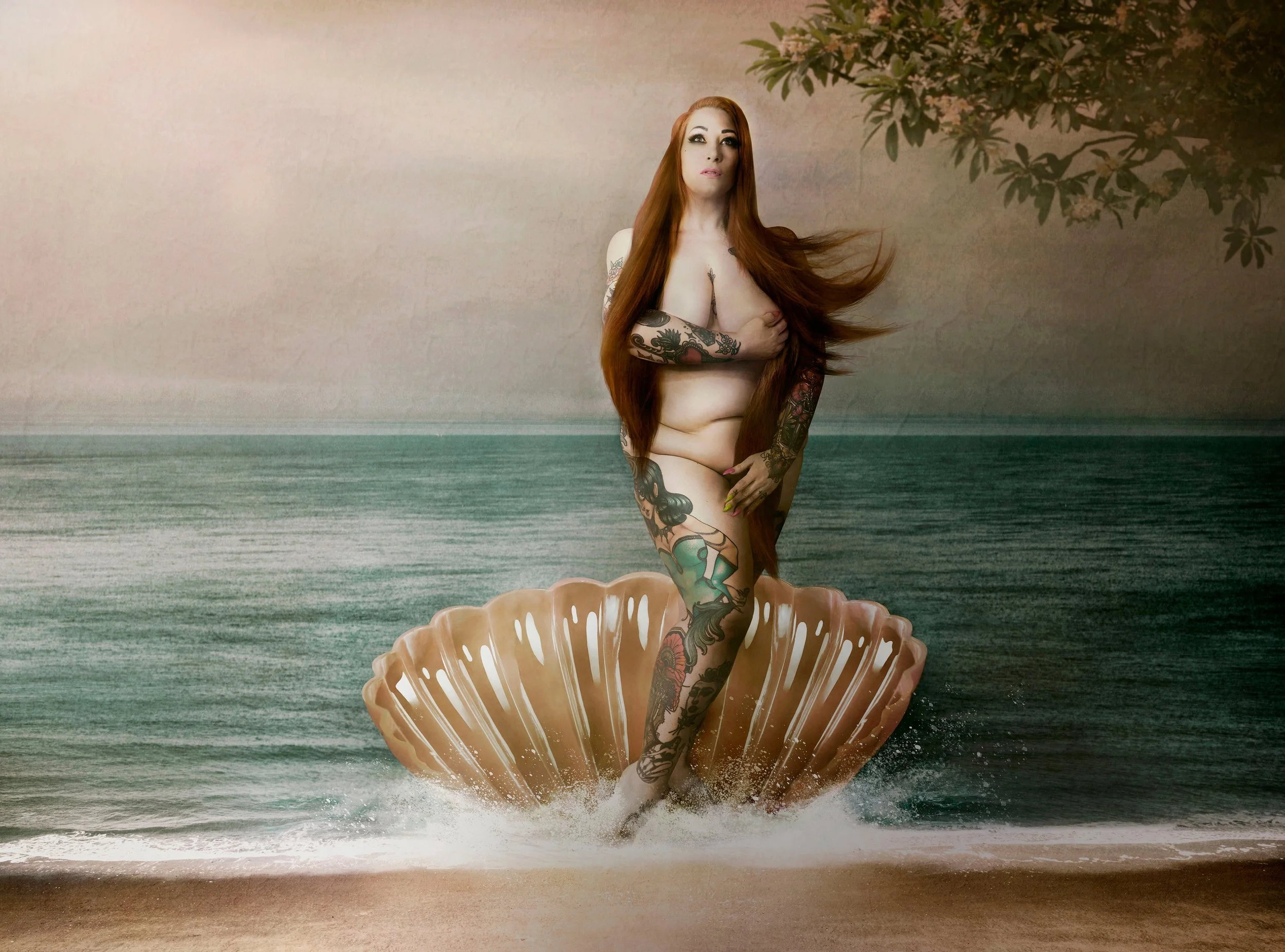 Une femme nue avec de nombreux tatouages se tient debout dans une coquille geante en bois dans une scène qui combine des éléments naturels et artistiques, avec un arrière-plan de mer et un arbre au-dessus.