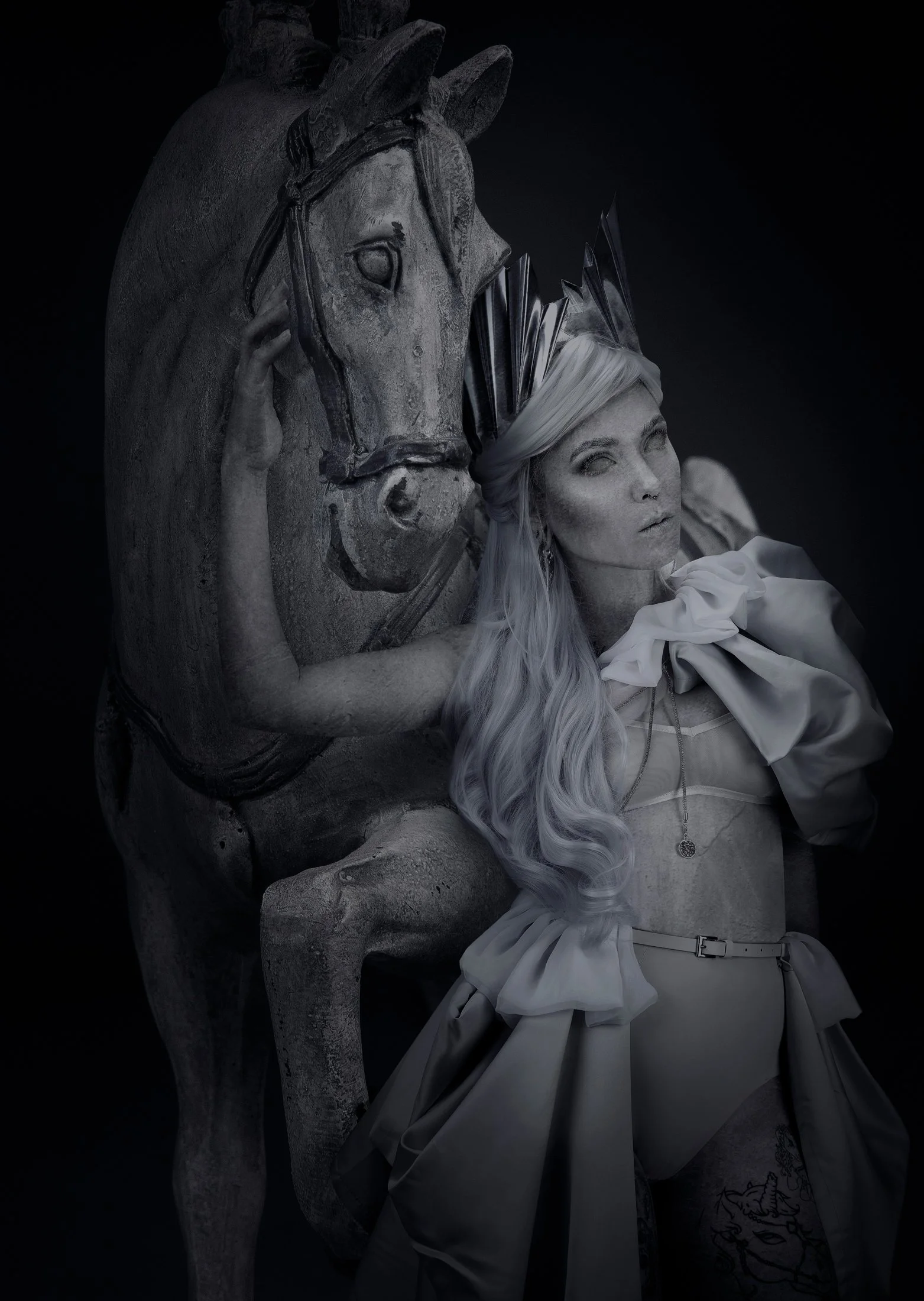 Une sculpture de cheval en pierre avec une jeune femme à côté, portant une robe et un collier, dans un style artistique noir et blanc.
