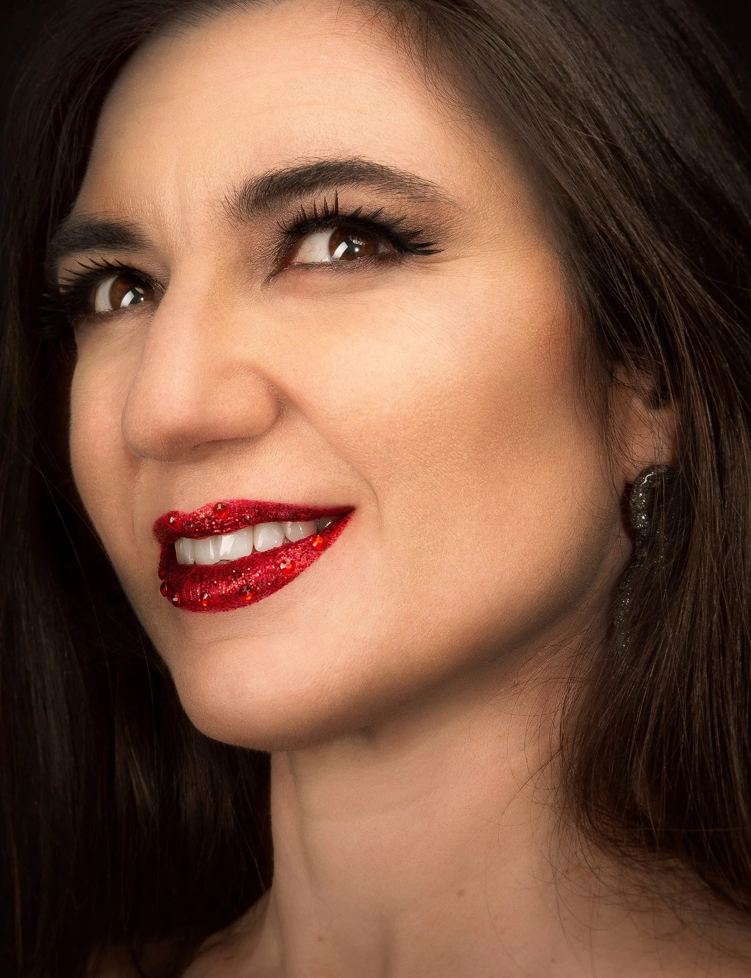 Close-up d'un visage féminin, montrant les yeux, le nez, les lèvres rouges, avec des cheveux bruns et une boucle d'oreille brillante