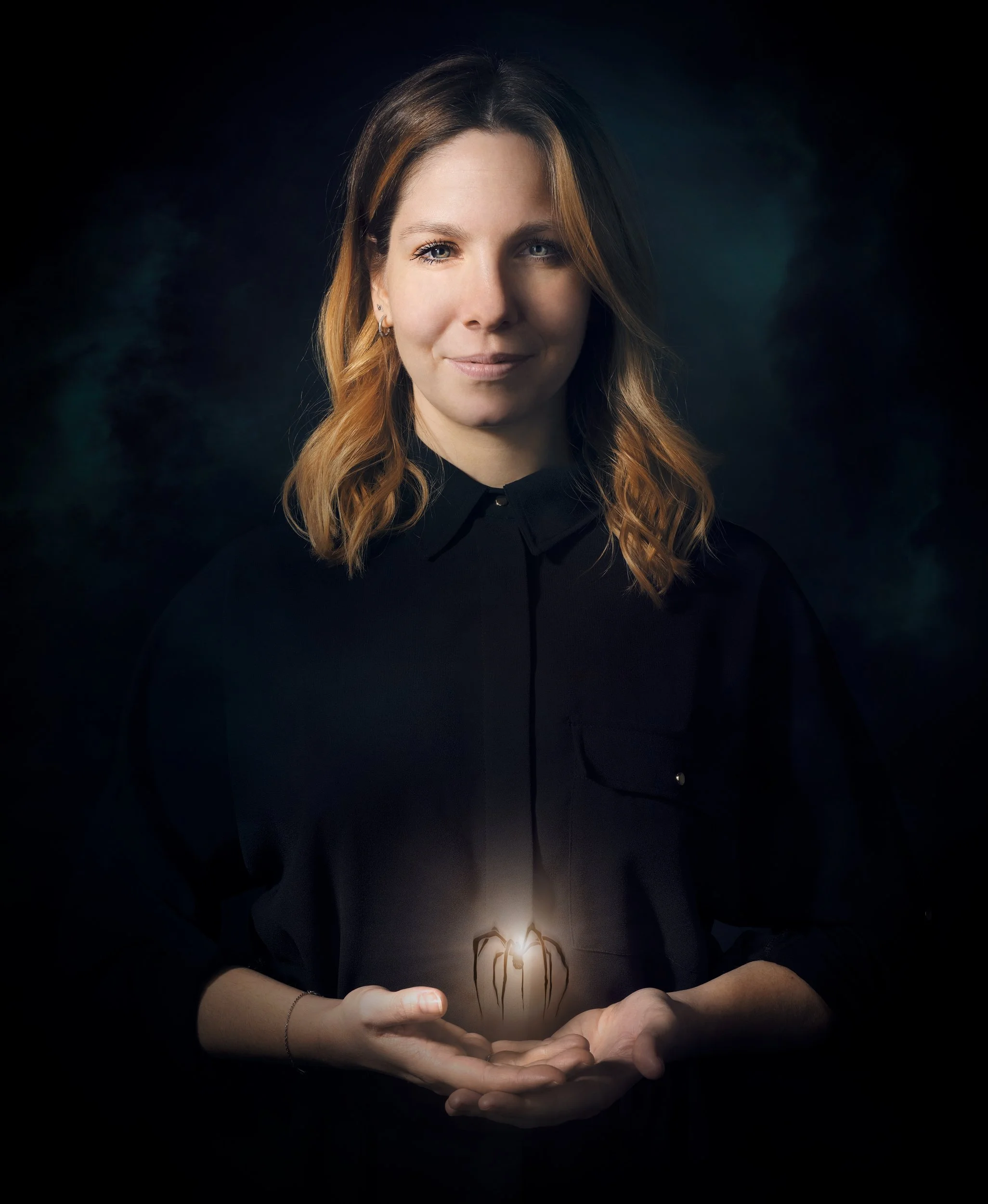 Une femme souriante tient une lumière dans ses mains, le fond est noir et l’éclairage met en valeur son visage et ses mains.