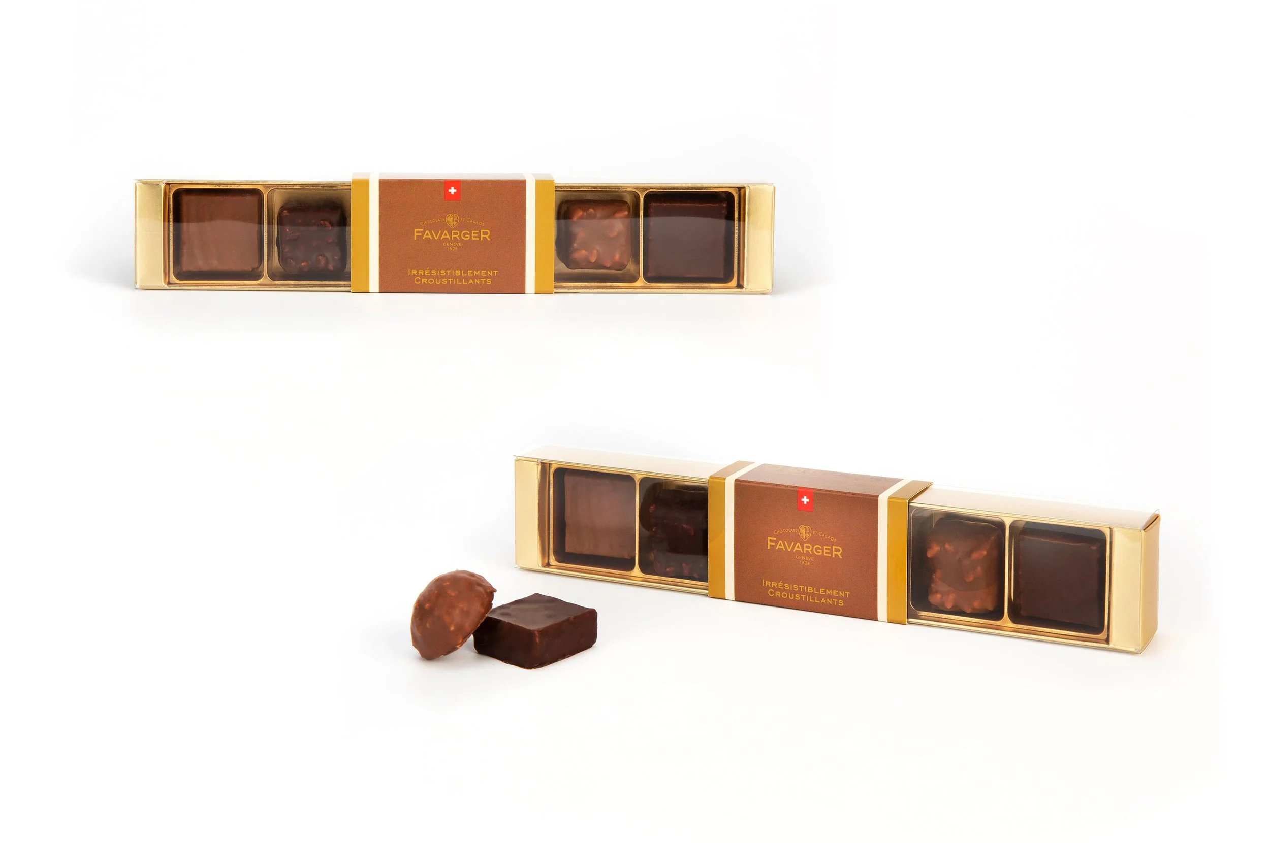 Une boîte de chocolats avec plusieurs carreaux de chocolat, certains avec des noisettes, à côté de deux morceaux de chocolat et une noisette.