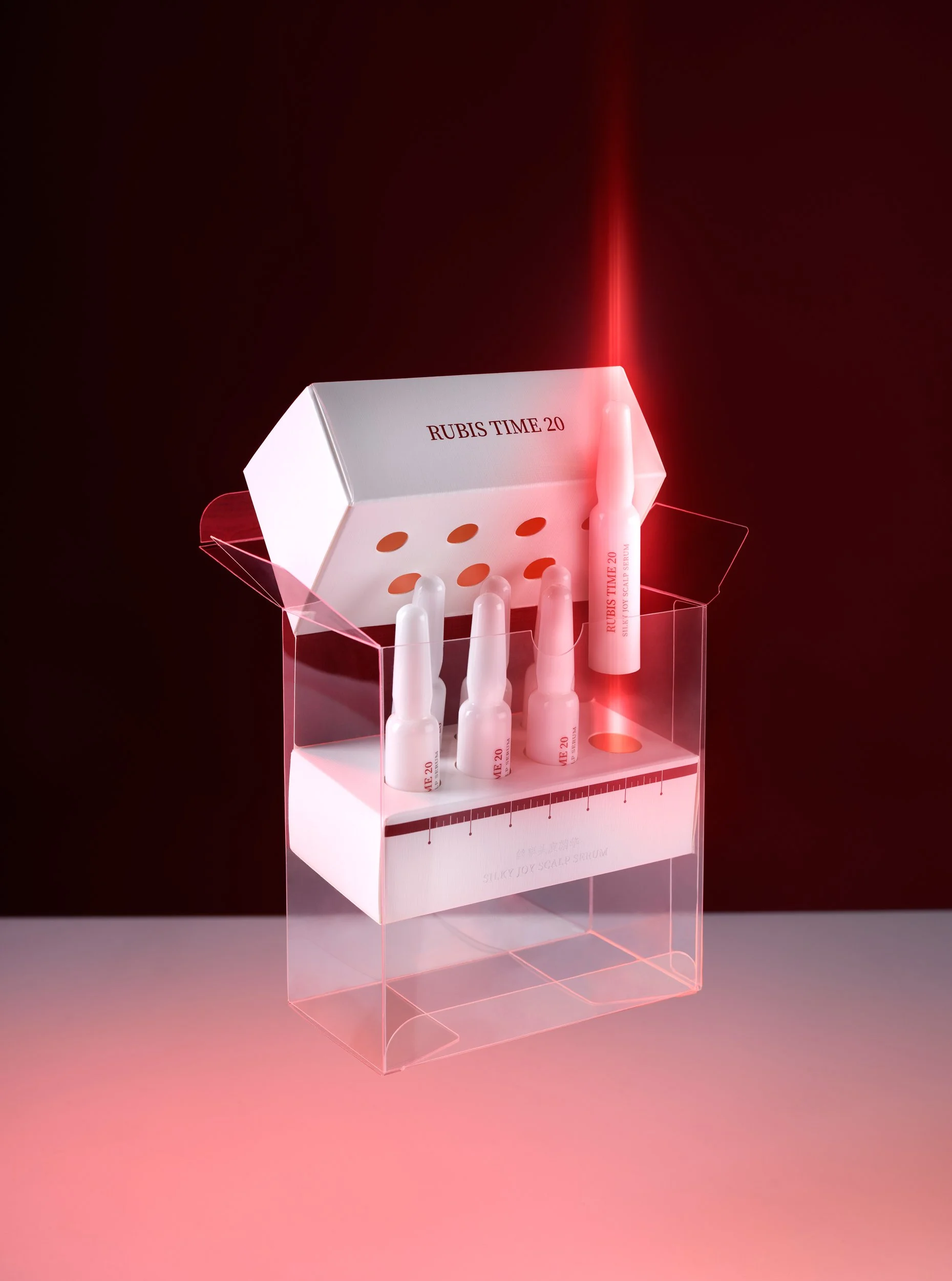 Boîte blanche avec des wrs pour injections, étiquetée 'RUBIS TIME 20', disposée dans un plateau en plastique transparent, sous un éclairage rouge sur fond noir