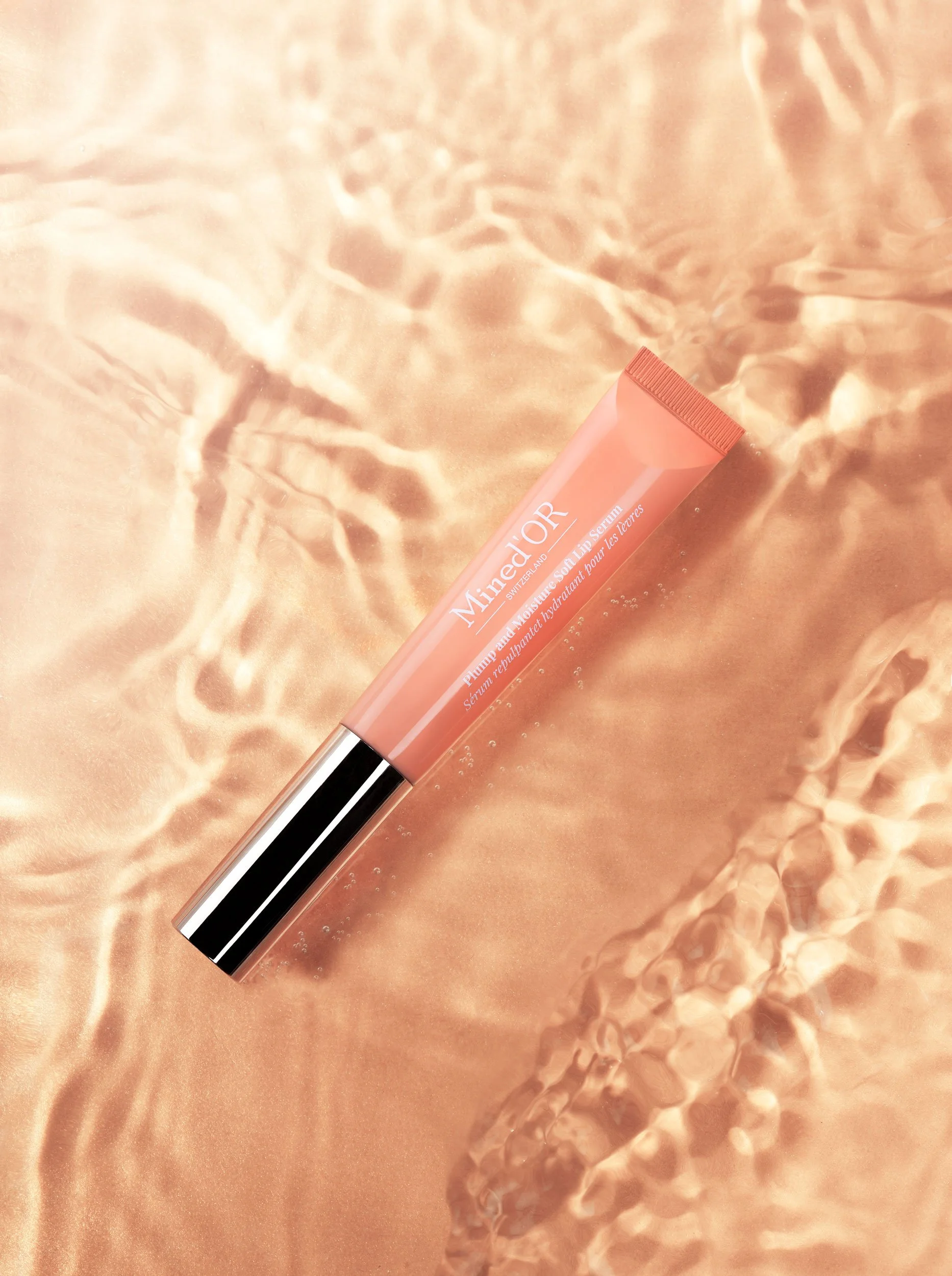 Un tube de baume à lèvres de la marque Dior posé sur une surface en tissu doré ou satinée avec des reflets de lumière.
