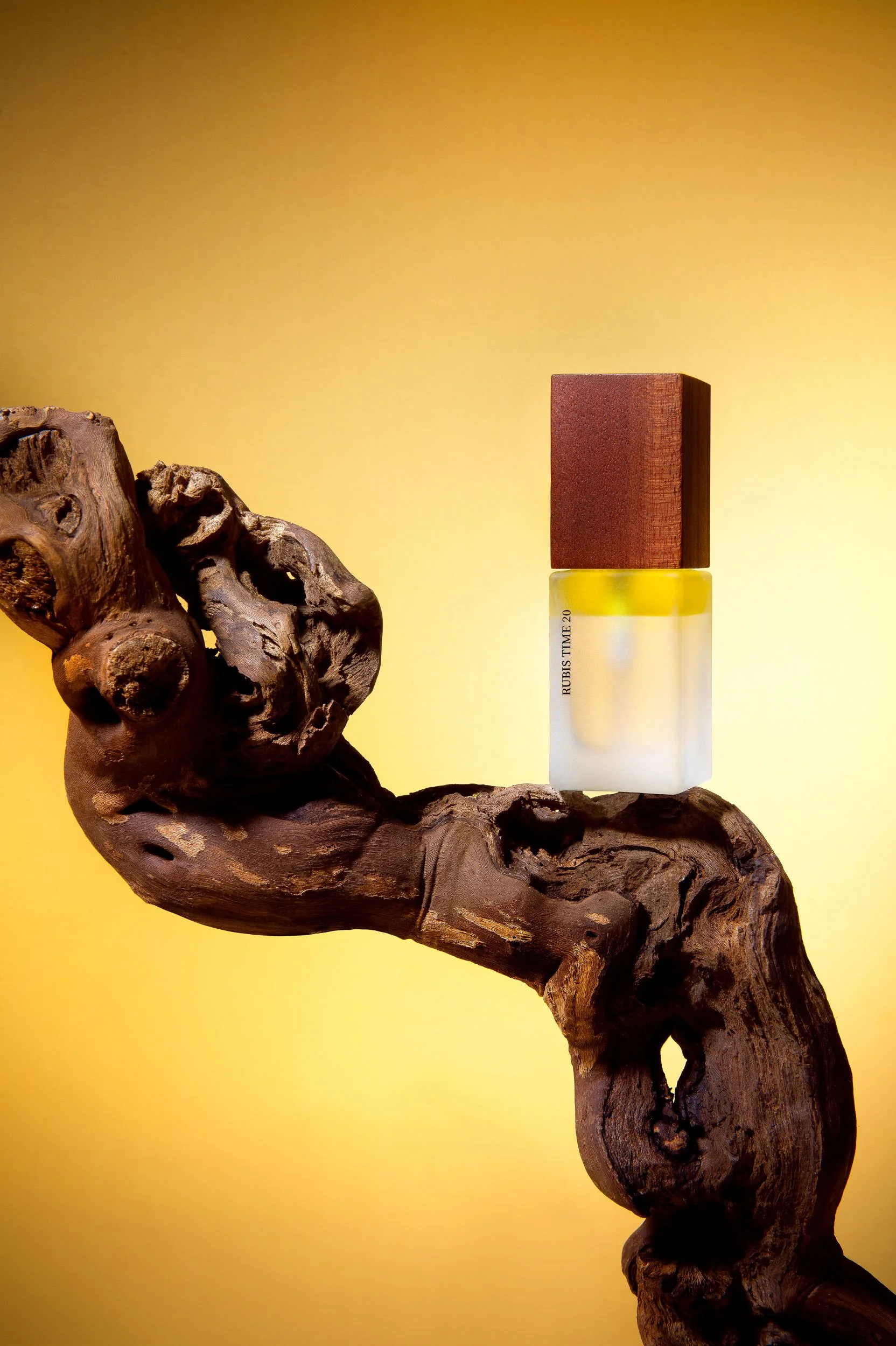 Une pièce de parfum avec un bouchon en bois rougeâtre, placée sur une branche de bois tordu et une surface jaune en arrière-plan.