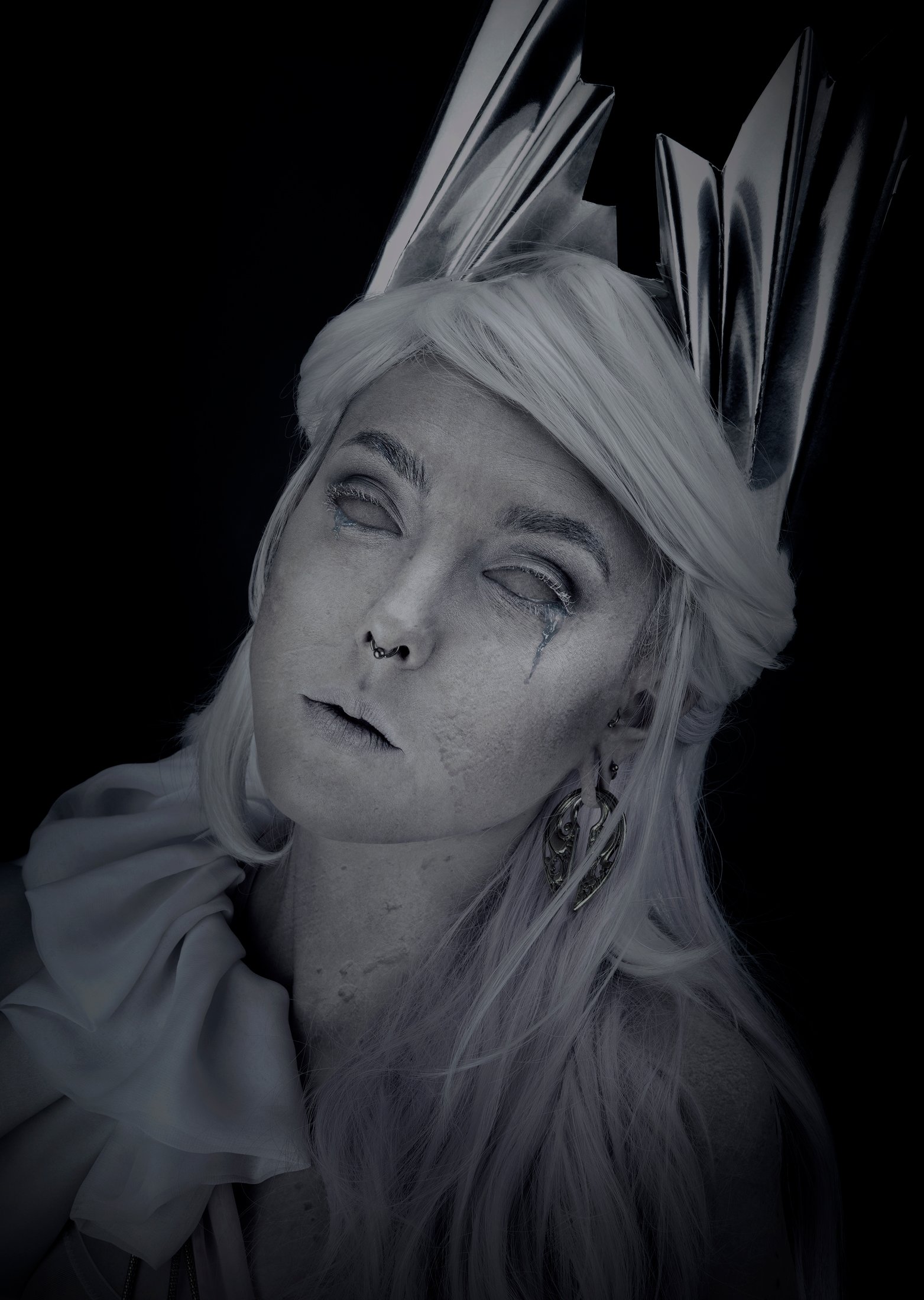 Photo en noir et blanc d'une femme avec une coiffure claire, portant un vêtement ample, avec des piercings, des bijoux et un regard pensif, dans un contexte artistique ou stylistique.