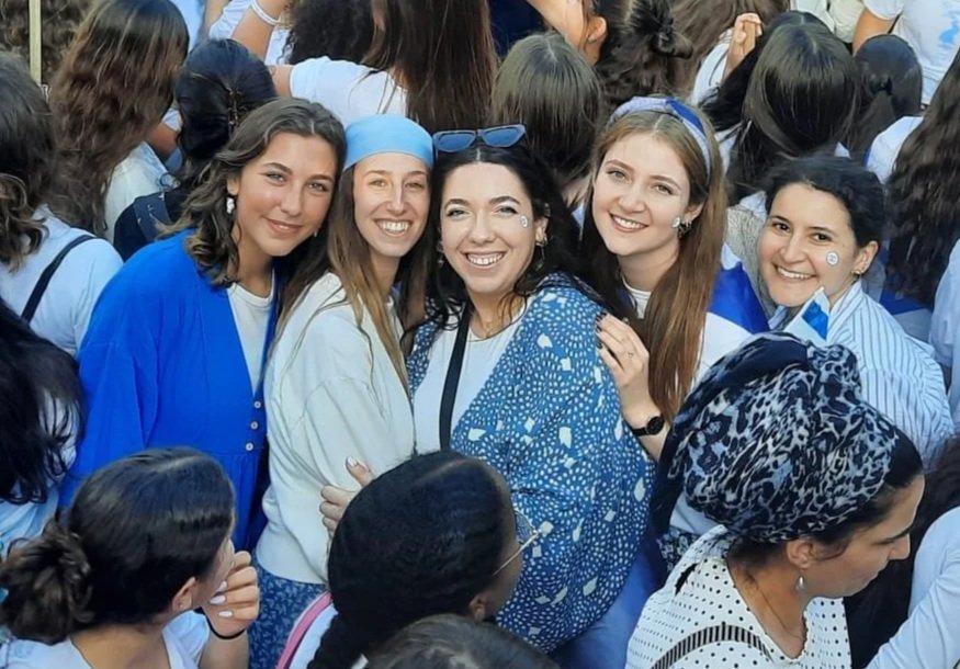 Group of women smiling and posing together among crowd at outdoor event.