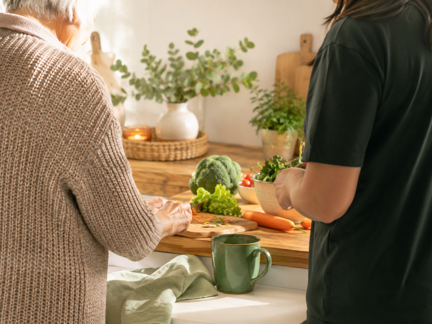 Two women chopping vegetables in a kitchen with potted plants and a wooden countertop.