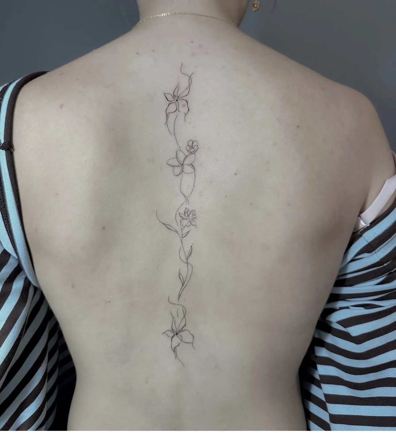 A person's upper back with a vertical line tattoo featuring a floral vine design.