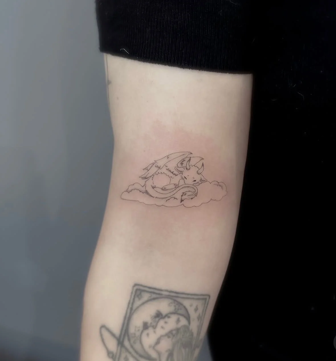 Tattoo of a unicorn with dragon wings on a person's forearm, lying on a cloud.