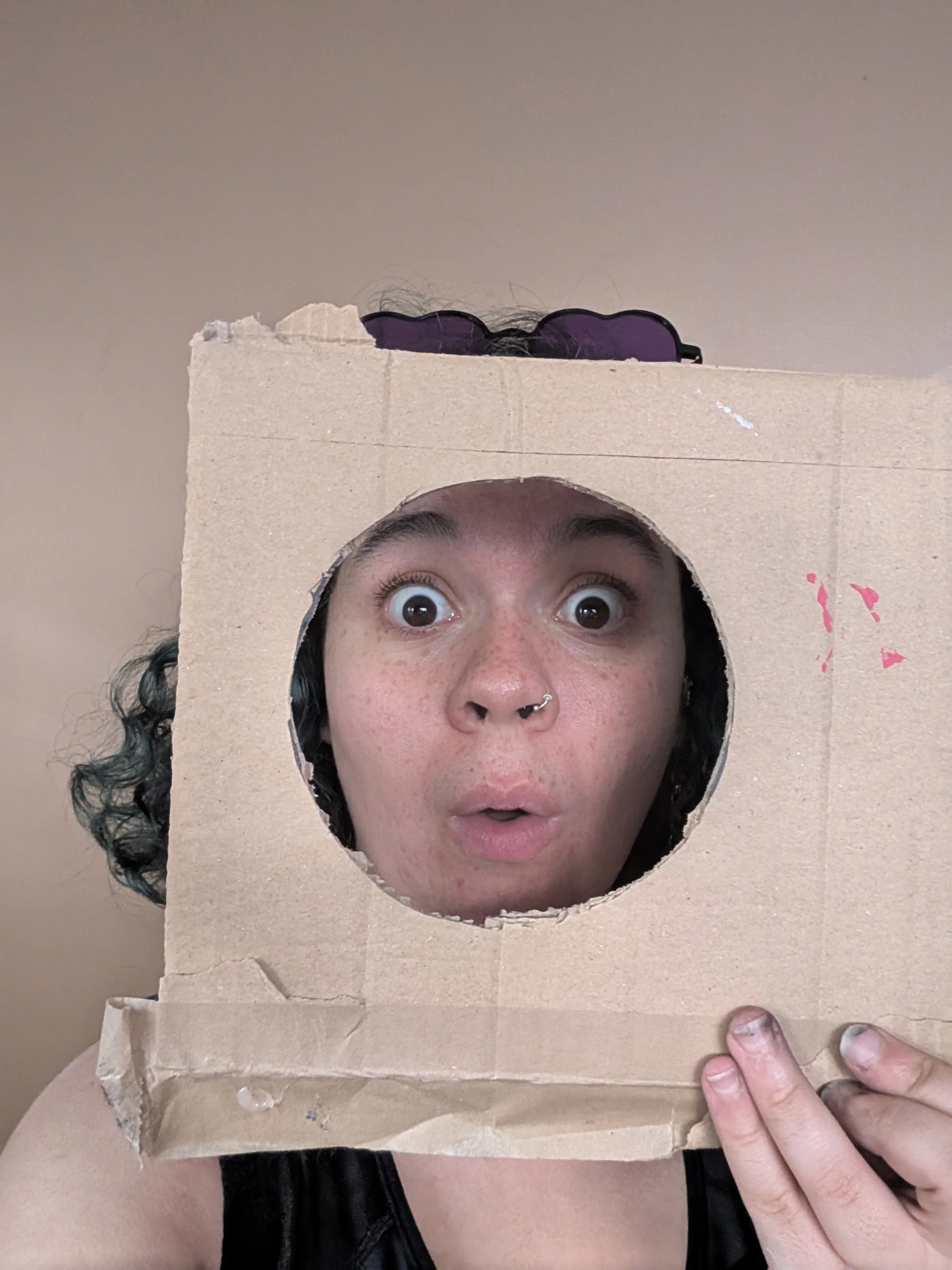 Rachael holding a cardboard box with a circular cutout showing their face.
