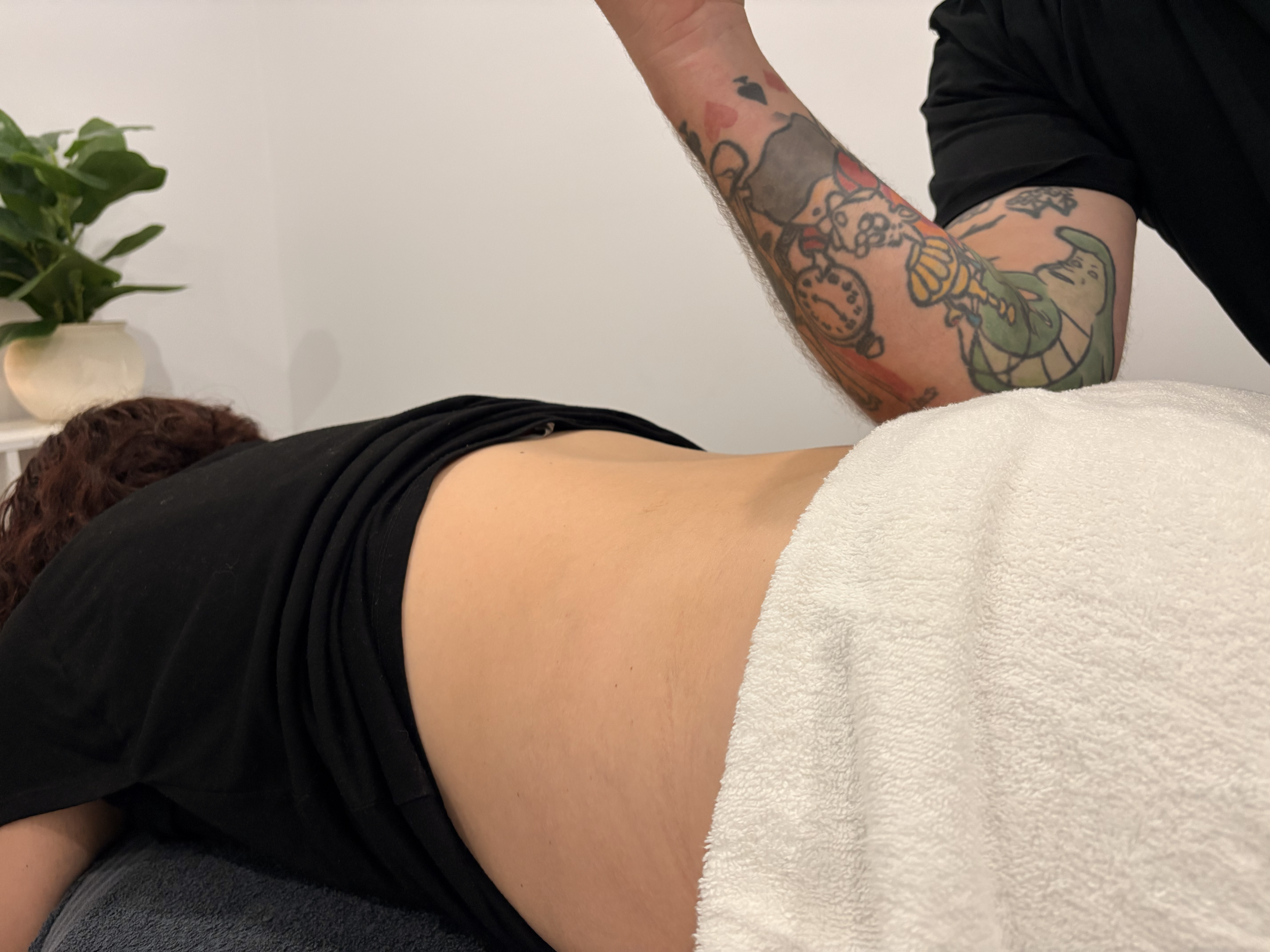 Tattooed arm performing a massage on a person lying face down on a massage table.