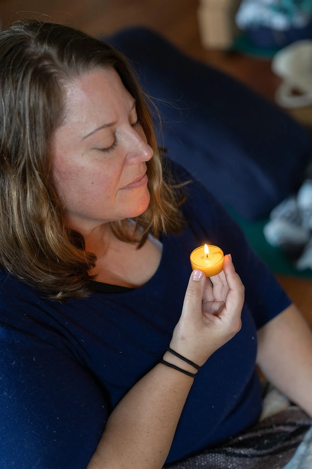 Woman with closed eyes holding a lit tealight candle.