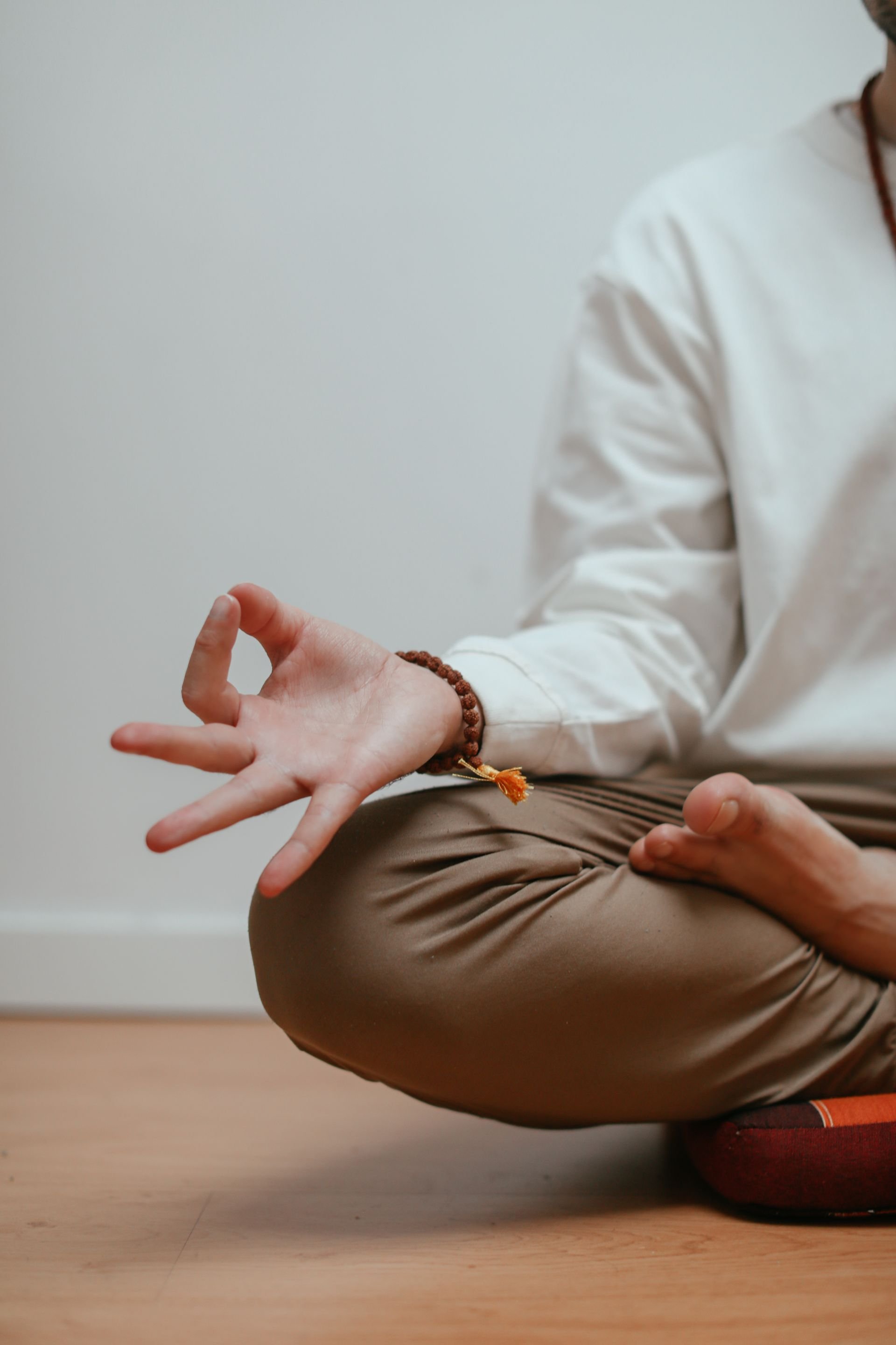 Person sitting cross-legged on the floor, practicing yoga or meditation, with hands forming a mudra gesture.