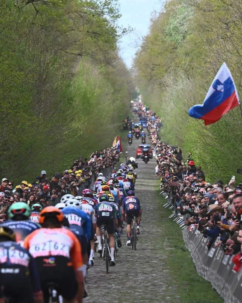 Une course cycliste avec de nombreux compétiteurs sur une route pavée, entourée de spectateurs et de drapeaux, dont le drapeau russe.