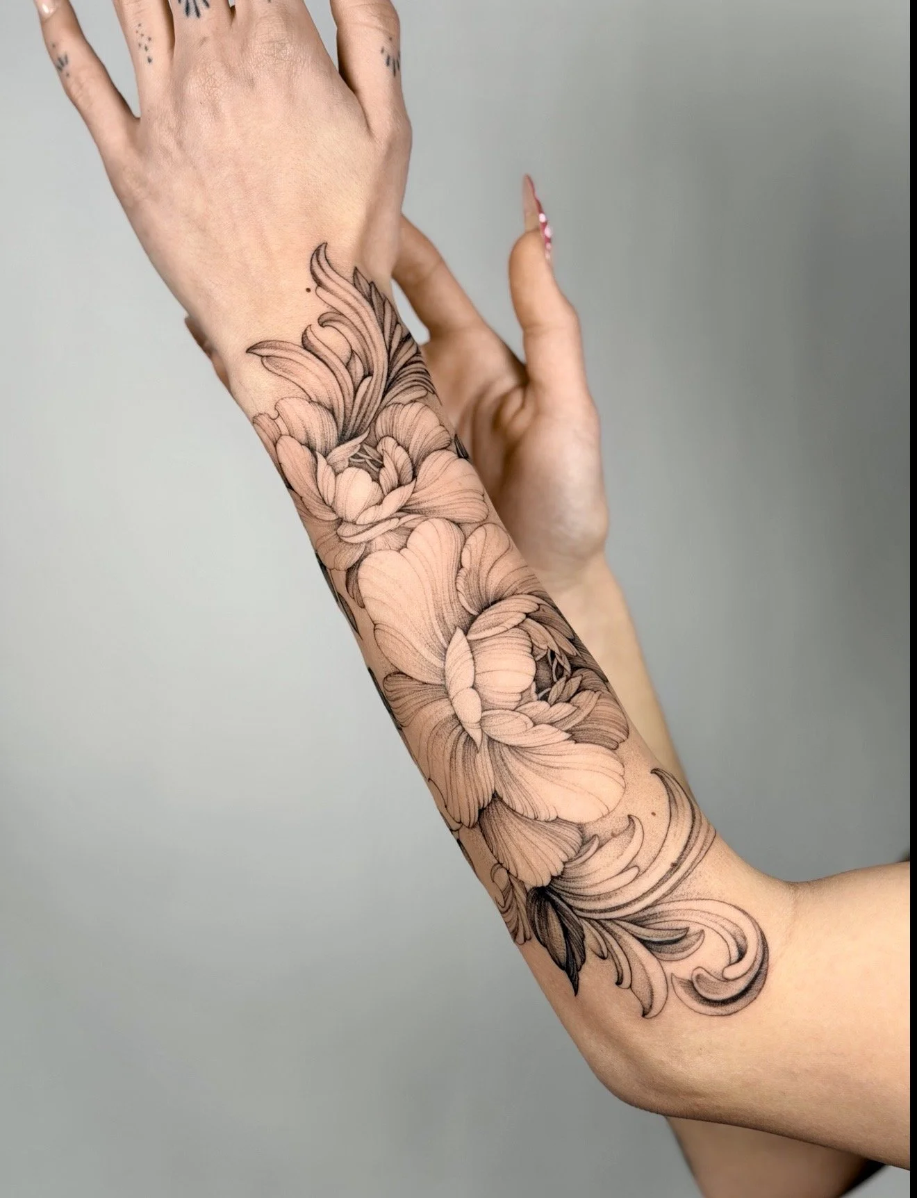 Close-up of a person's arm and hand, with the arm covered in an intricate black and gray floral tattoo.