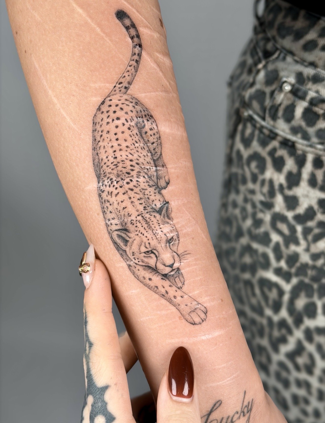 A tattoo of a cheetah on a person's forearm, depicting the cat in a walking stance with detailed spots and facial features.