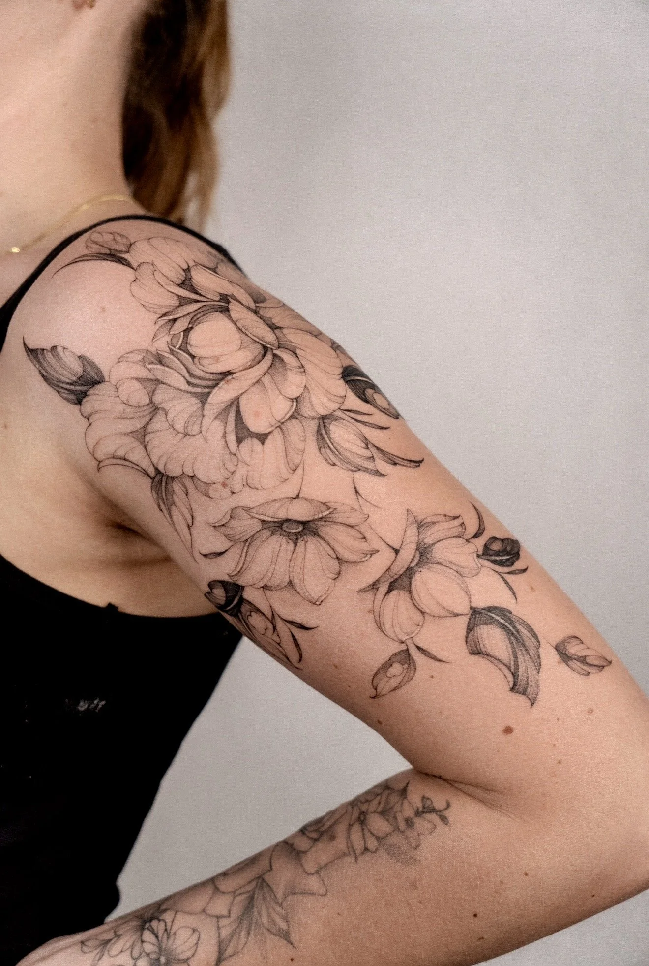 Close-up of a person's upper arm with a large black and gray floral tattoo, showing detailed petals and leaves, against a plain background.