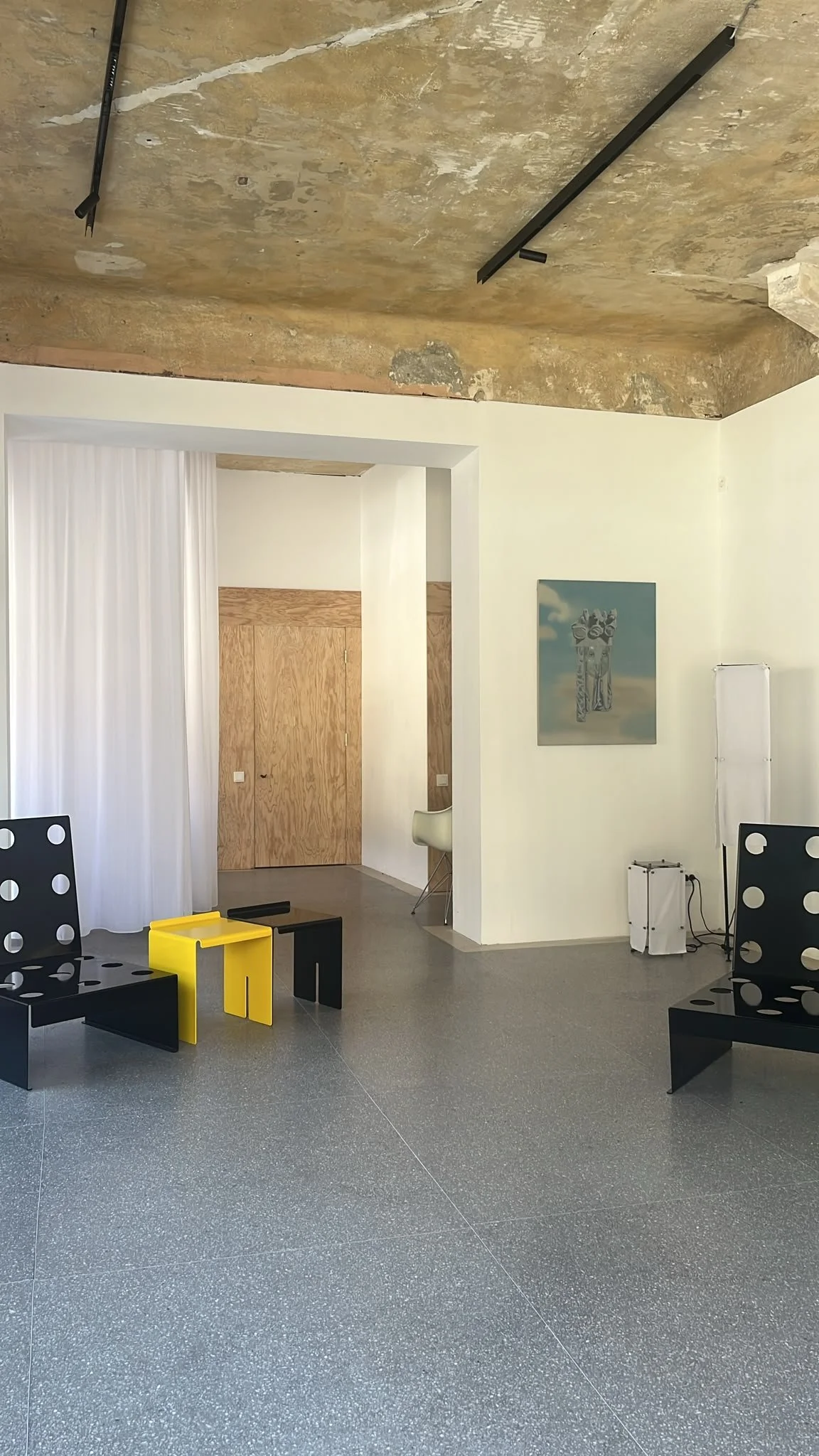 Modern interior space with black and yellow stools, white curtains, wooden sliding door, artwork on the wall, and polka dot chairs in the foreground.