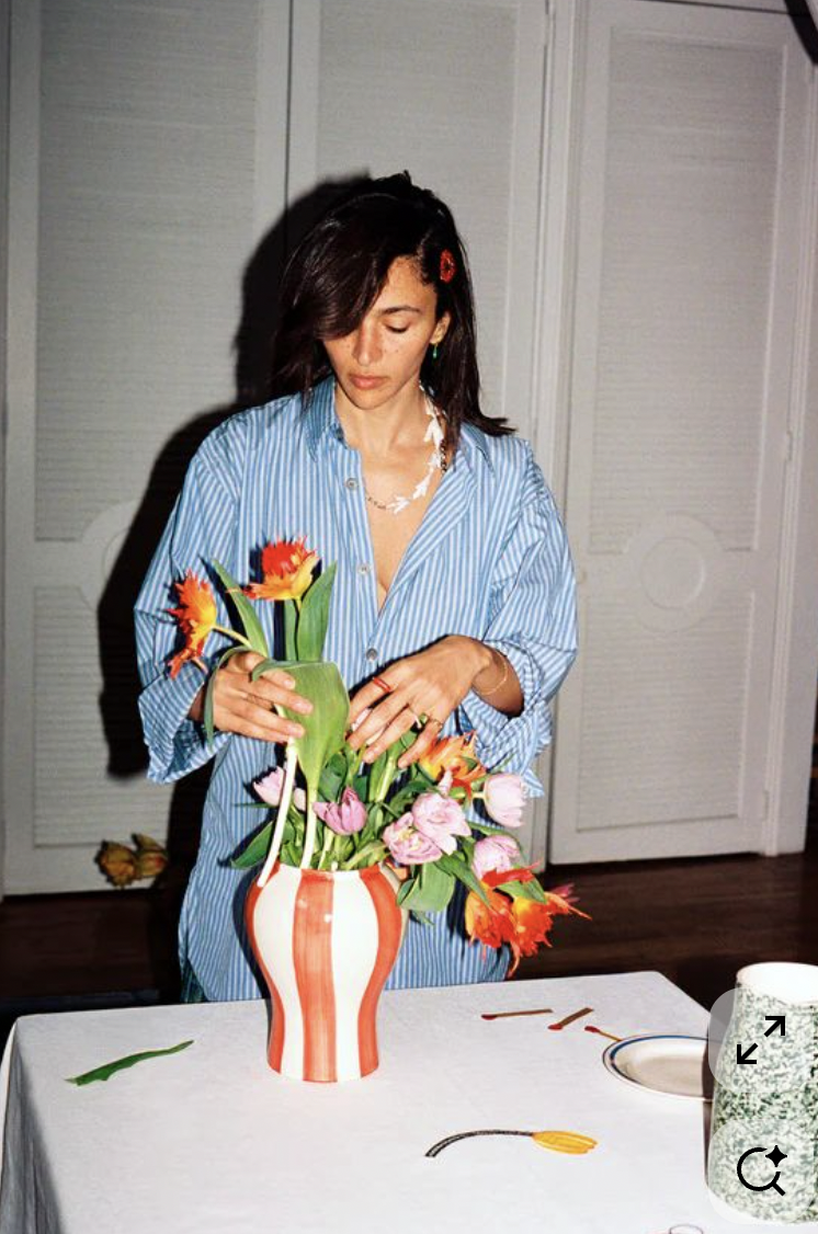 A woman arranging a bouquet of flowers in a striped vase on a table.
