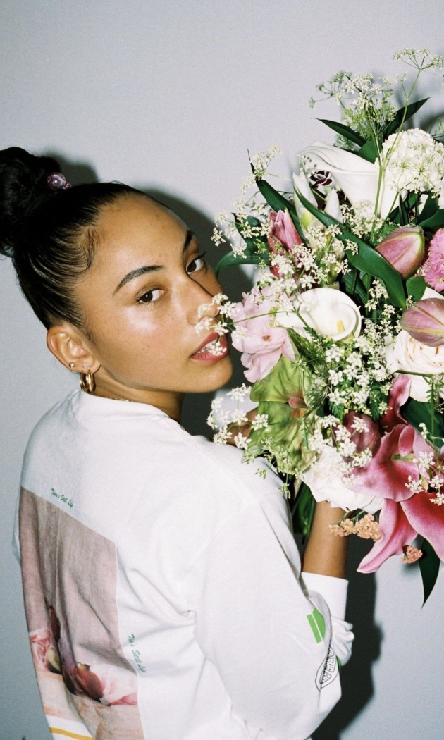 Woman holding large bouquet of pink, white, and purple flowers with green foliage, looking over her shoulder at camera.